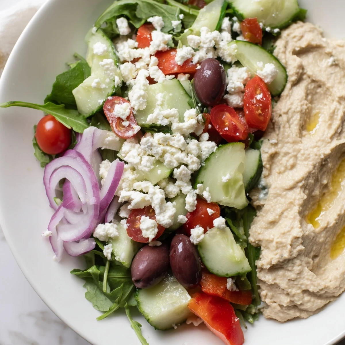 Creamy hummus crowns a fresh Mediterranean Salad with Hummus, mixing cucumber, tomatoes, and lemon dressing on a rustic platter.