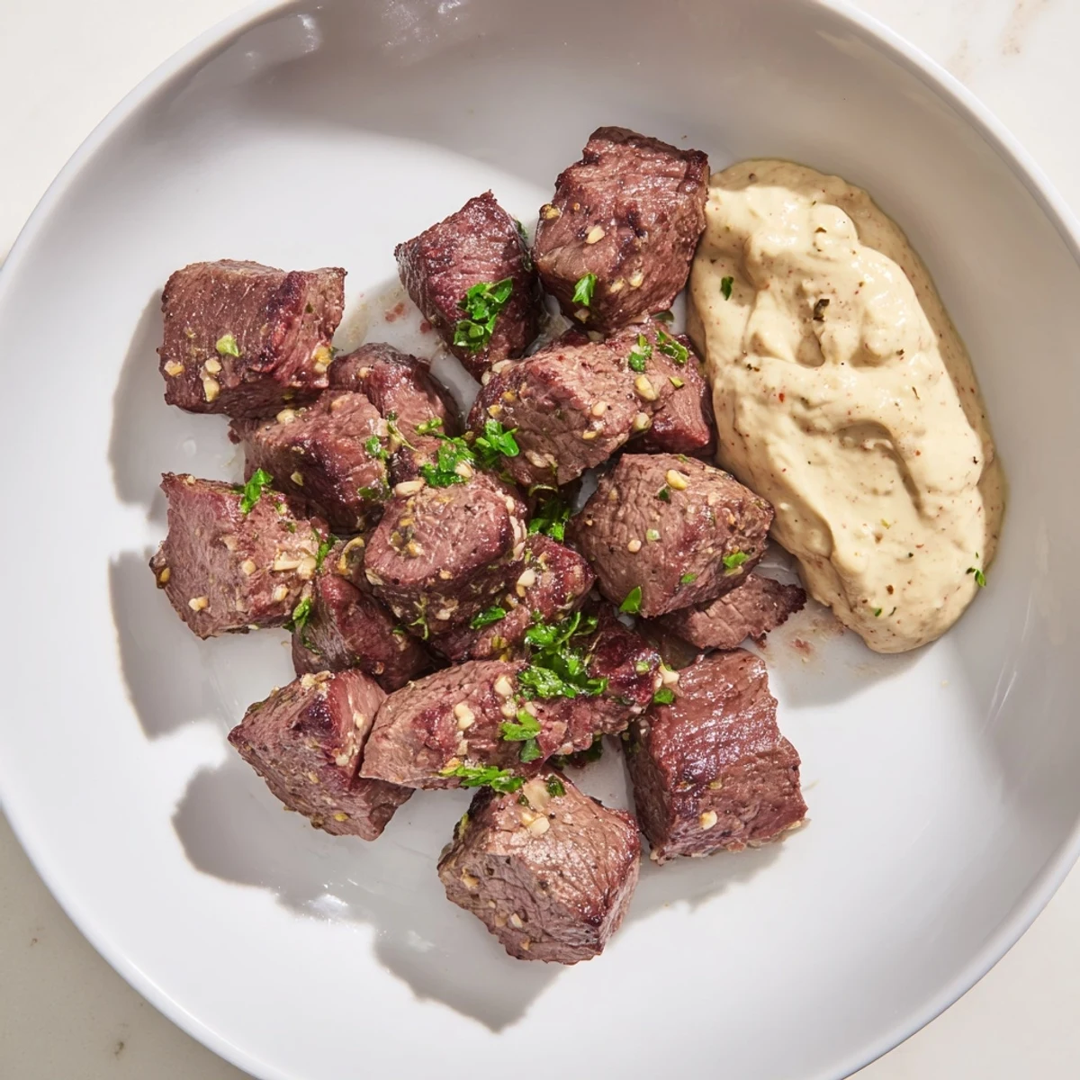 Golden-brown steak bites sizzling in a skillet with melted garlic butter, served alongside a creamy horseradish dipping sauce.  