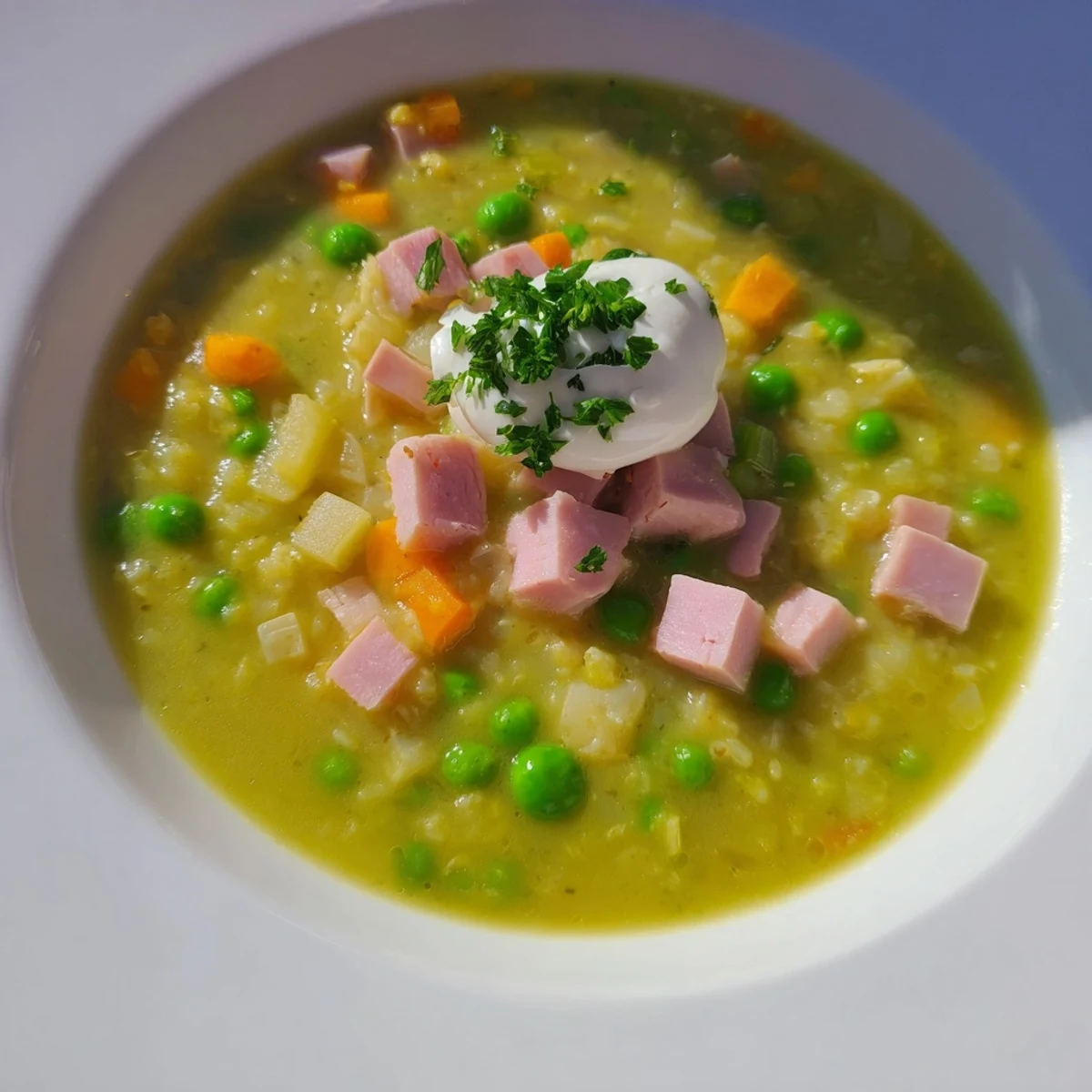 A bowl of Spring Pea Soup with Ham and Turkey garnished with fresh parsley and a dollop of crème fraîche, served with crusty bread.