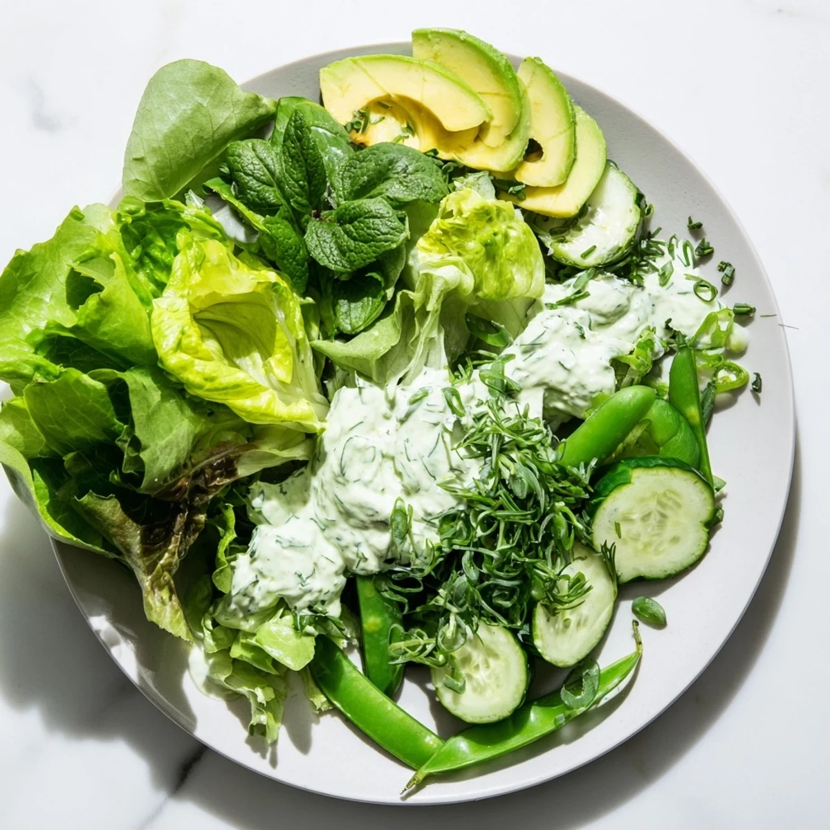 Vibrant mixed greens and crisp cucumber slices glistening with creamy Green Goddess dressing, topped with avocado and fresh herbs.