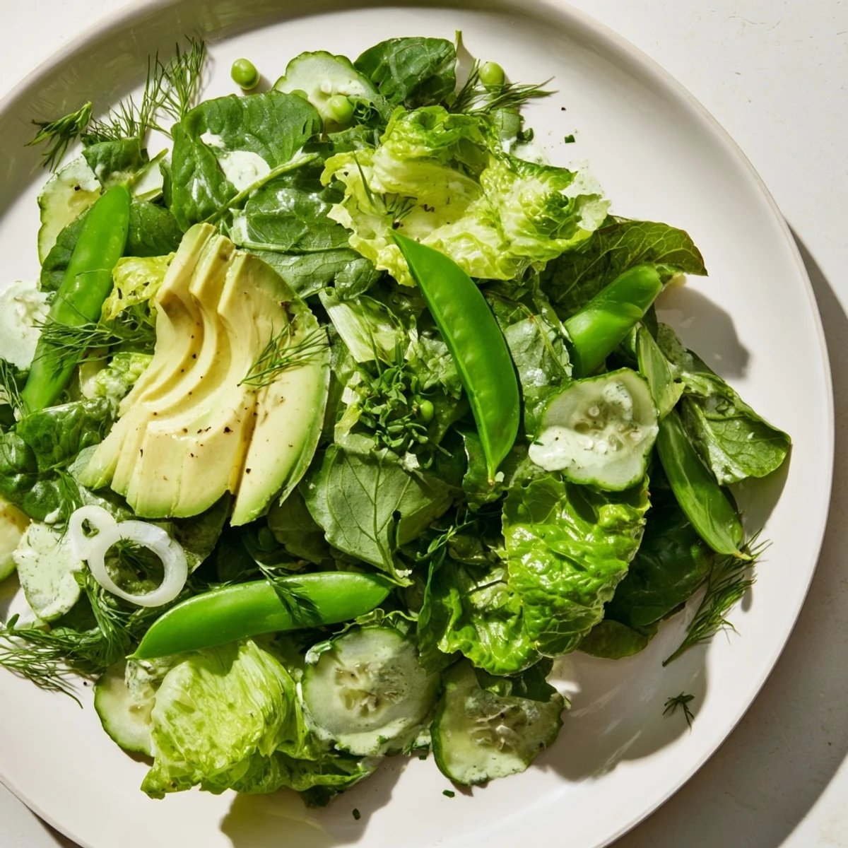 Fresh Green Salad with Green Goddess Dressing on a plate with creamy avocado slices, cucumbers, and snap peas.