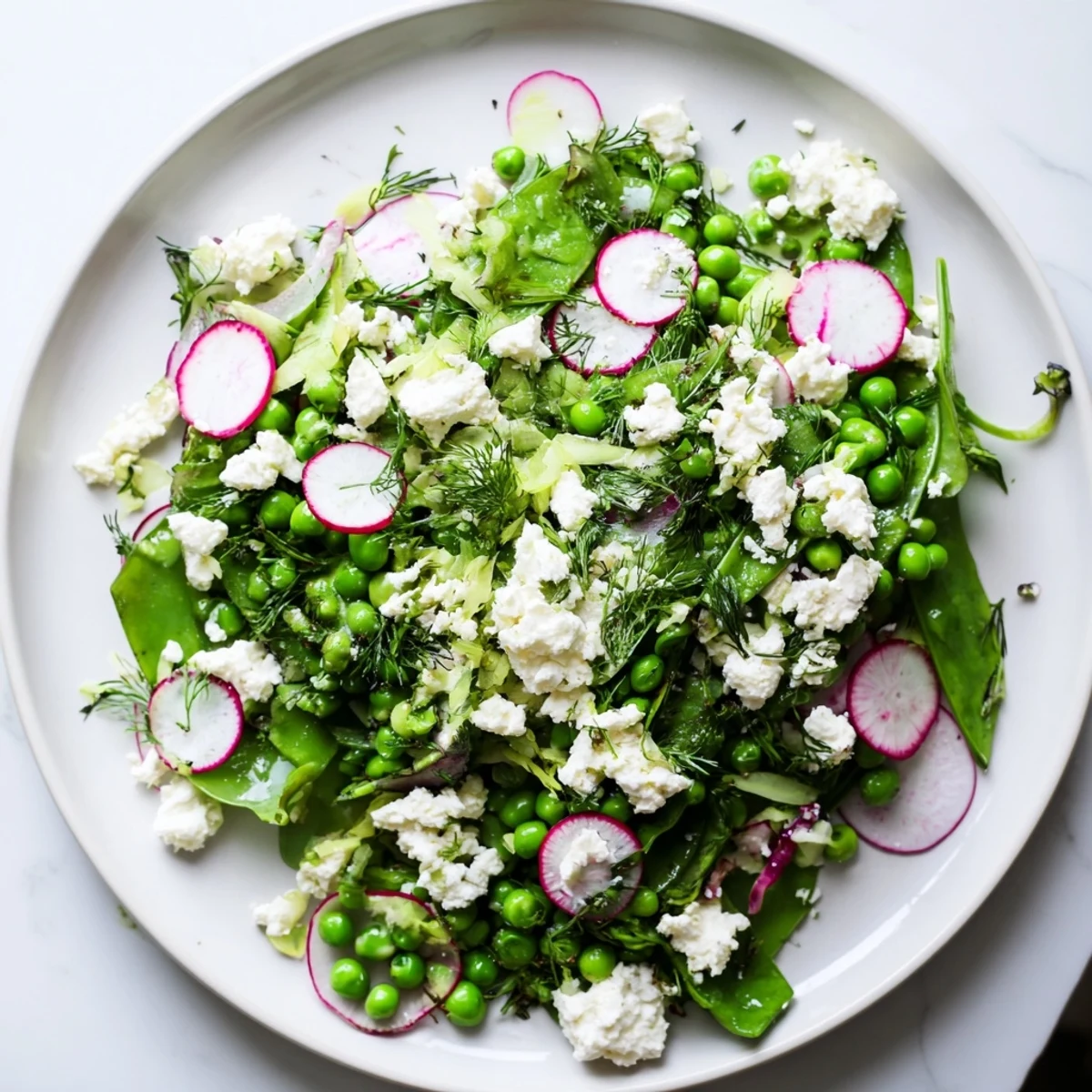 Freshly tossed Spring Pea Salad with Radishes and Feta on a rustic plate, garnished with mint and a lemon wedge.