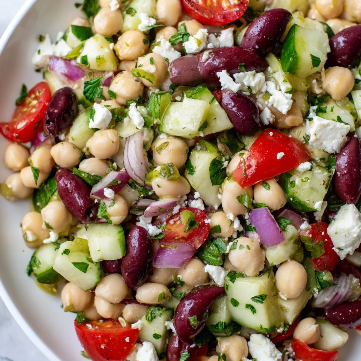 Fresh Mediterranean Dense Bean Salad with cucumber, tomatoes, and olives, topped with crumbled feta and dressed in a lemony vinaigrette.
