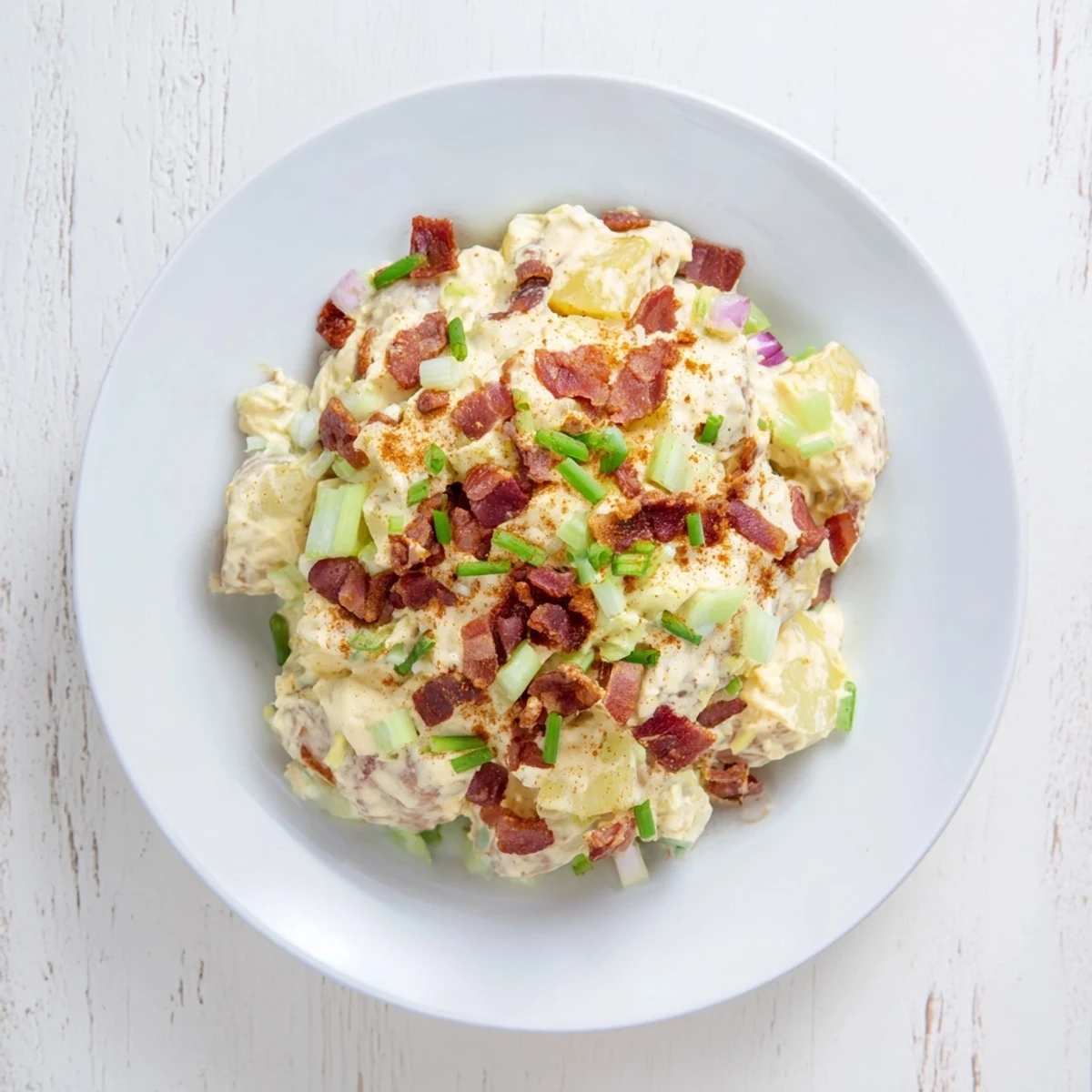 A chilled bowl of Steakhouse Potato Salad garnished with paprika, perfect alongside grilled steak for a hearty summer meal.