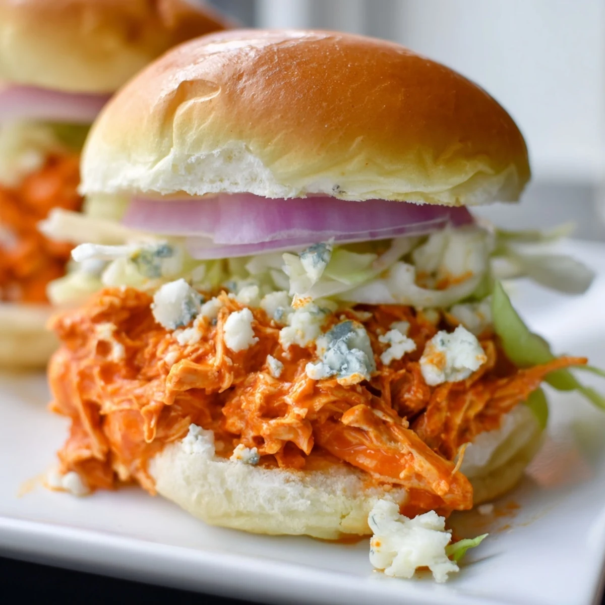 A close-up view of Spicy Buffalo Chicken Sliders stacked on a platter with celery sticks, ready for a game day gathering.