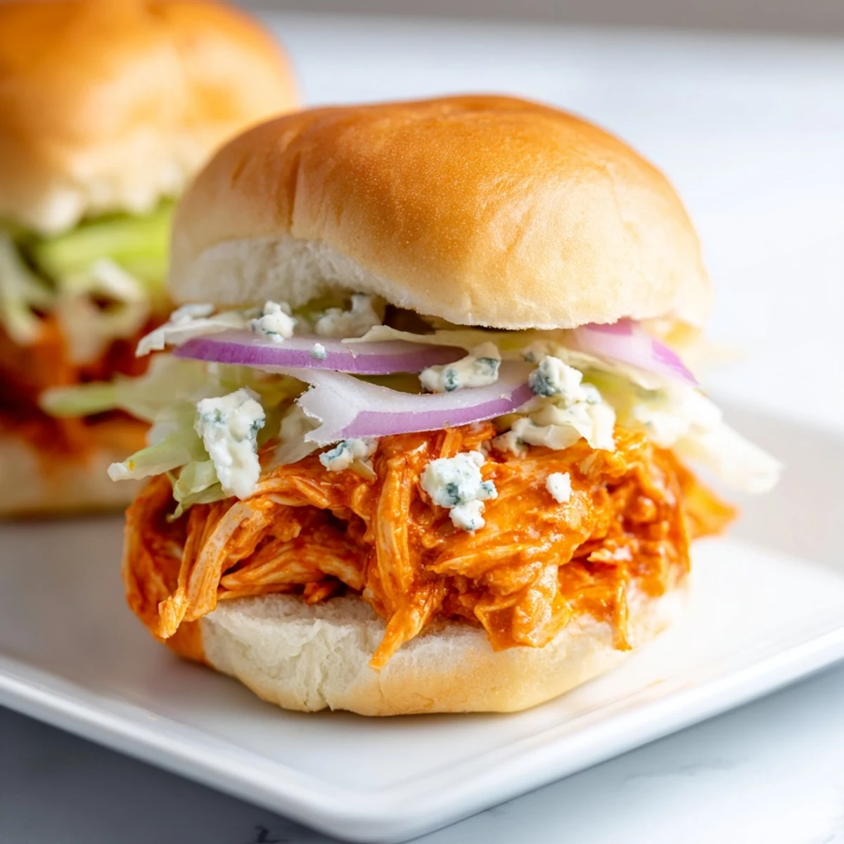 Spicy Buffalo Chicken Sliders feature tender shredded chicken in spicy sauce, topped with blue cheese and crisp lettuce on toasted buns.