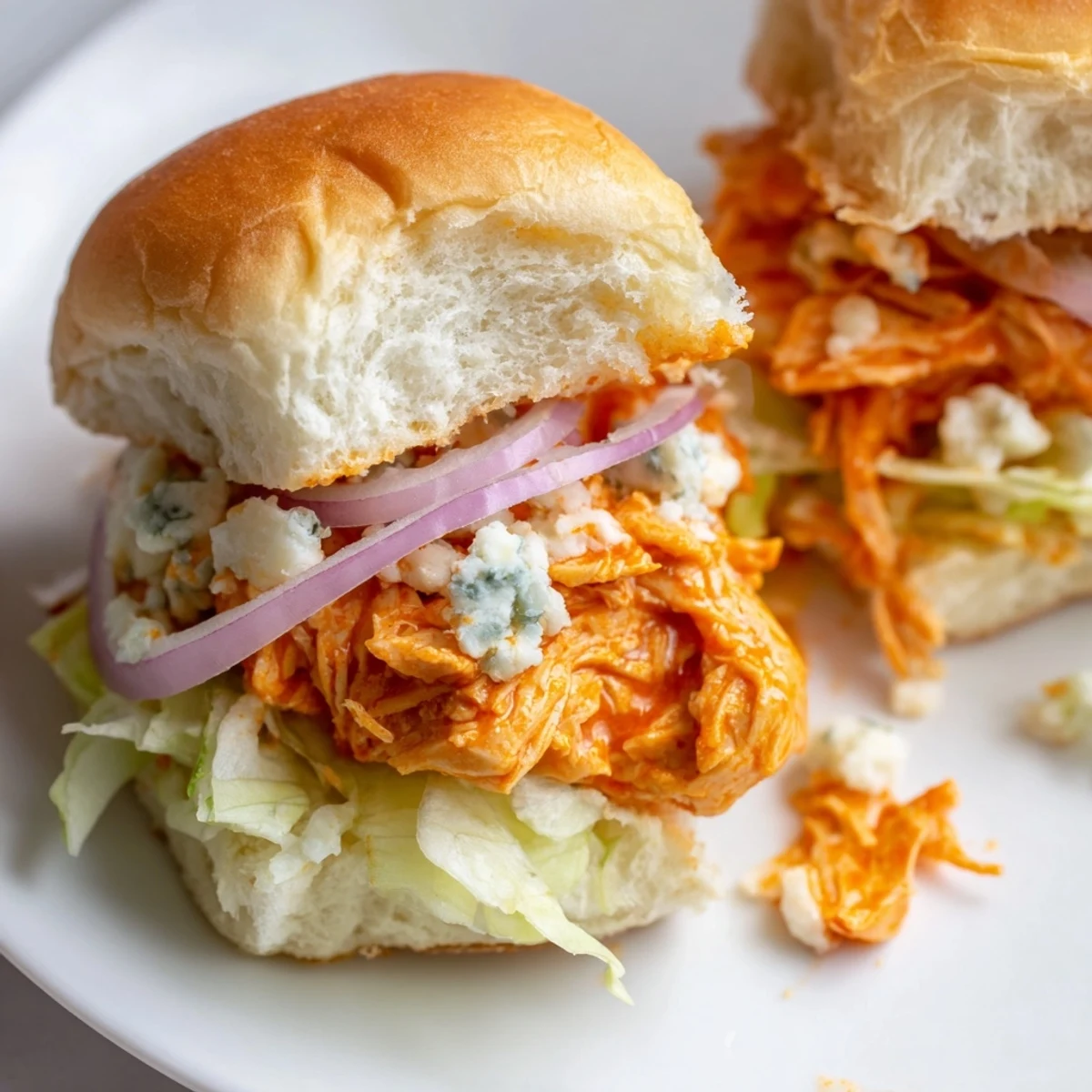 Freshly baked Spicy Buffalo Chicken Sliders with melted blue cheese, red onion, and chives on soft buns, served on a rustic board.