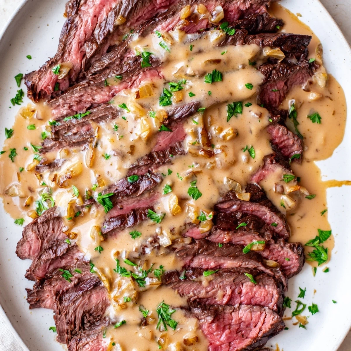 Sliced flank steak with roasted garlic sauce drizzled over, paired with steamed green beans and roasted potatoes on a rustic table.