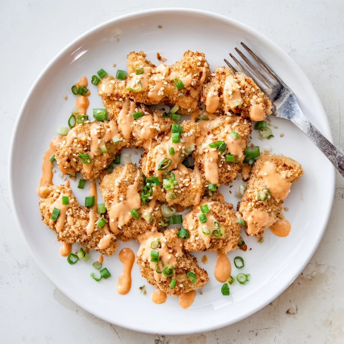 Crispy baked Quick Low Carb Bang Bang Chicken bites drizzled with creamy bang bang sauce, garnished with sesame seeds and sliced green onions.