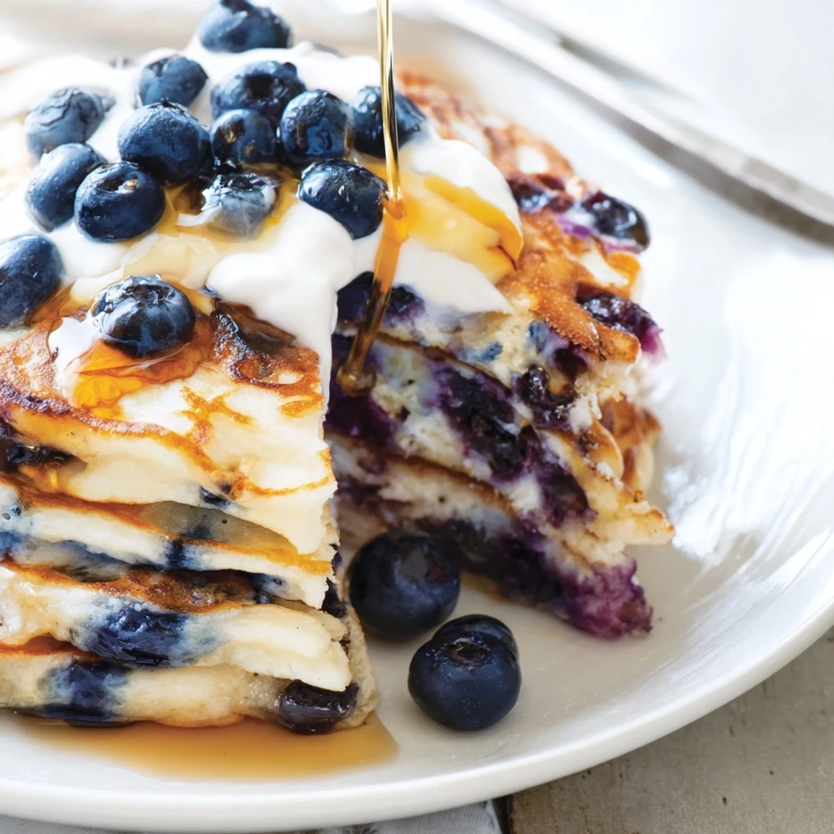 Plate of fluffy Greek yogurt blueberry pancakes topped with extra yogurt and blueberries