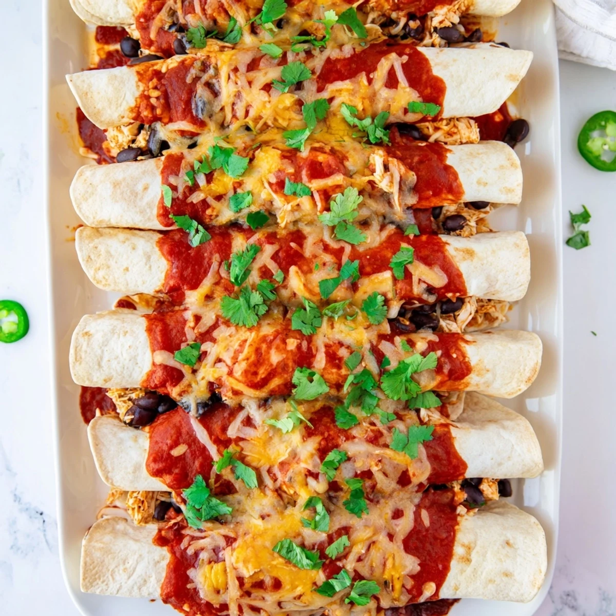Baked chicken enchiladas garnished with fresh cilantro and jalapeño slices after baking until bubbly and golden