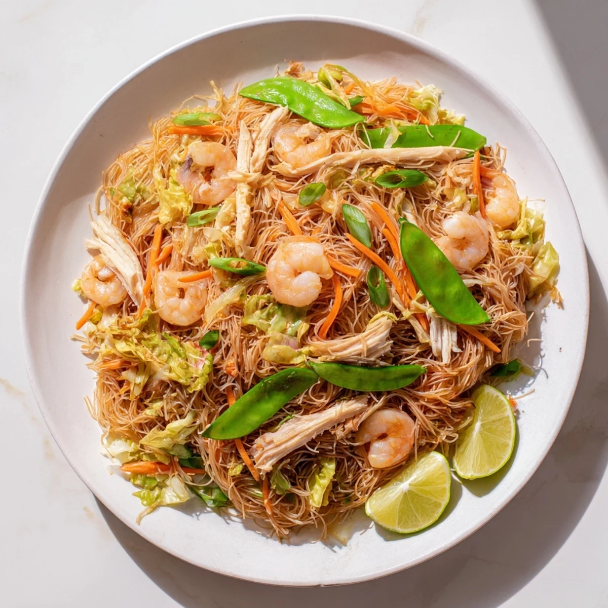 Steaming plate of Traditional Pancit Bihon featuring tender rice noodles stir-fried with succulent chicken shrimp and crisp julienned carrots