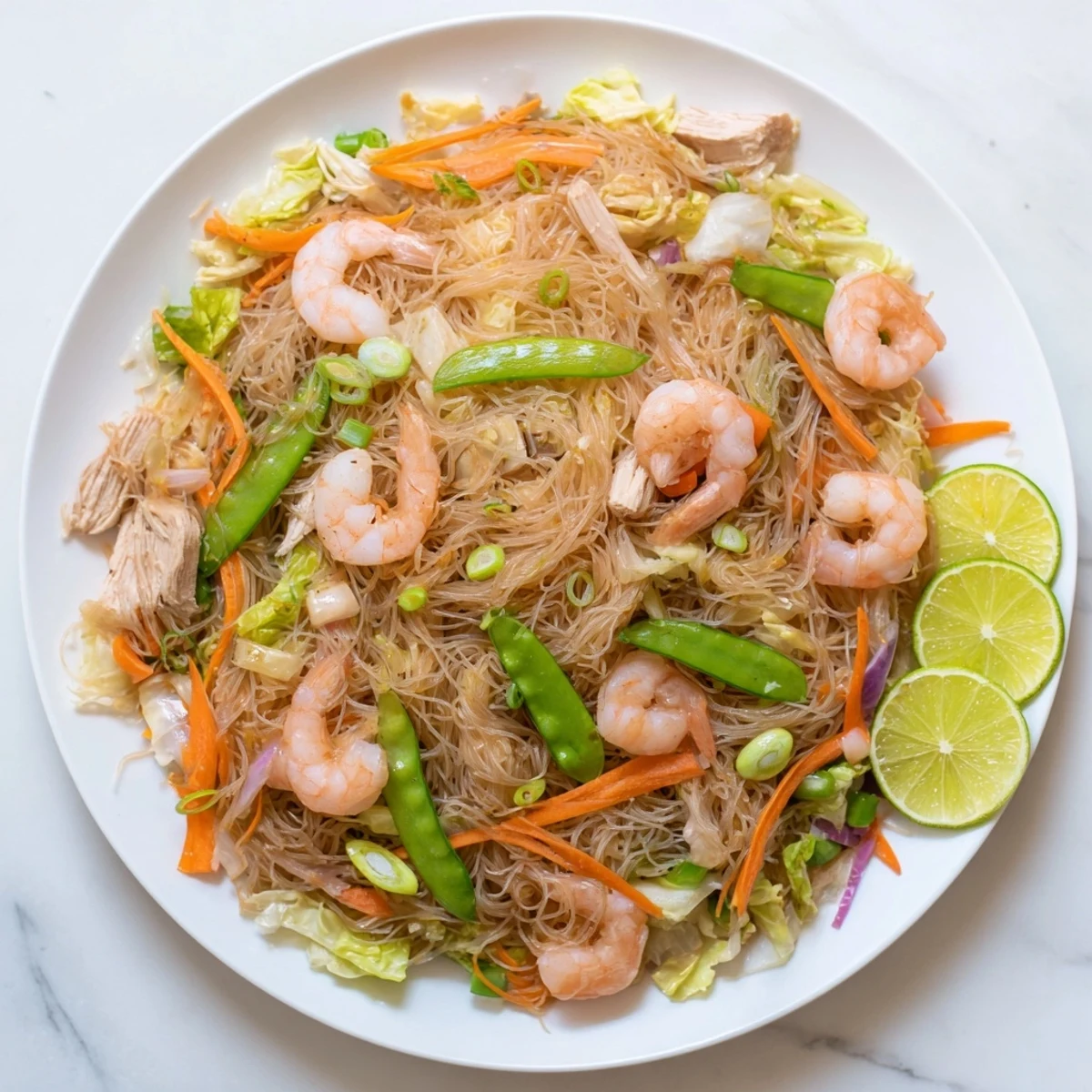 Family-style Traditional Pancit Bihon garnished with chopped green onions and served alongside bright lemon wedges for squeezing