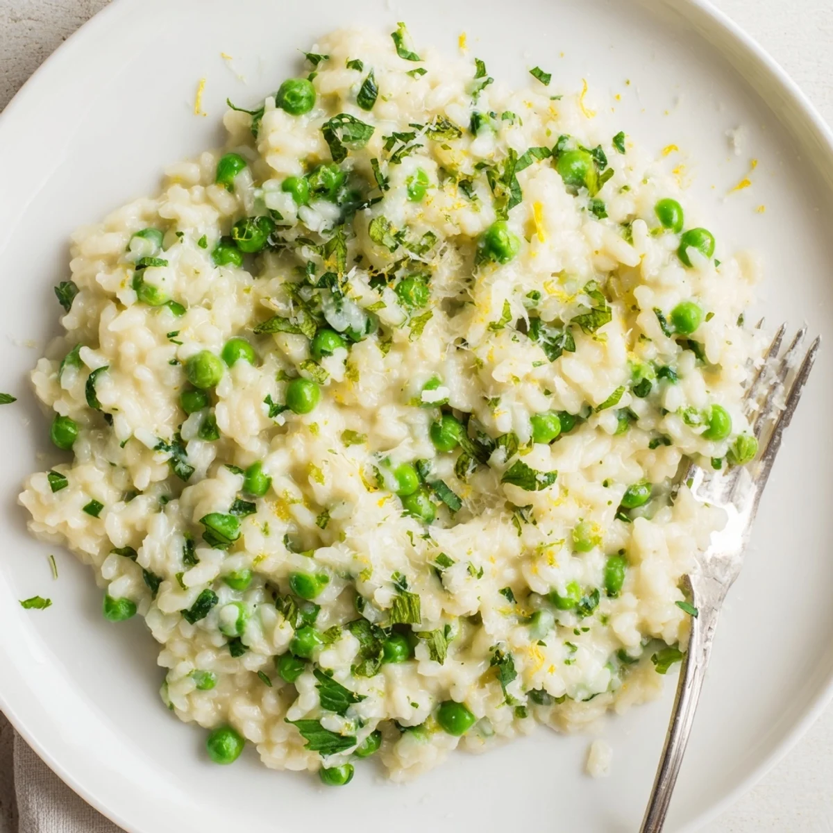 Creamy spring pea risotto topped with grated Parmesan and fresh green herbs in a white bowl