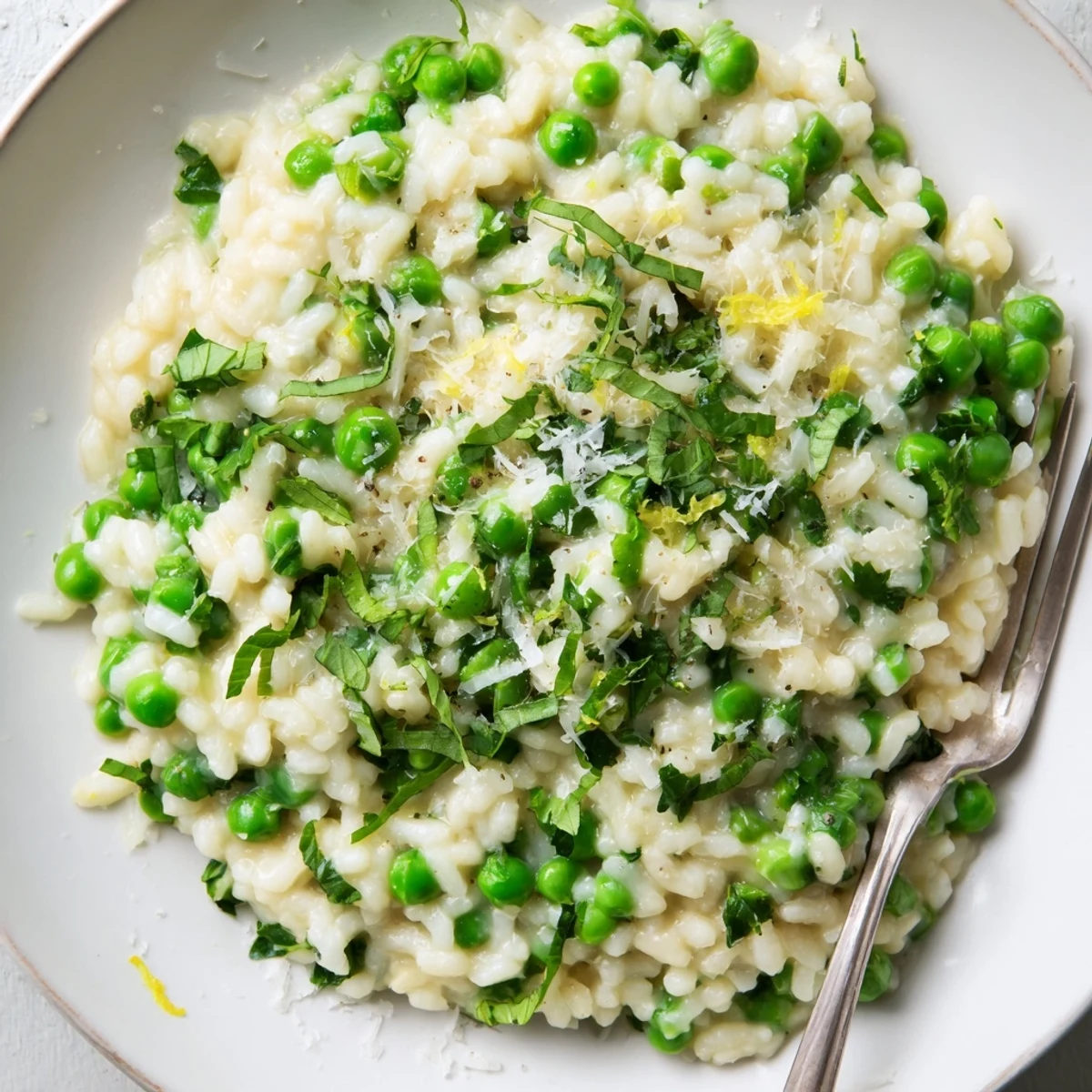 Spoonful of tender pea risotto sprinkled with parsley and extra Parmesan on a rustic wooden table