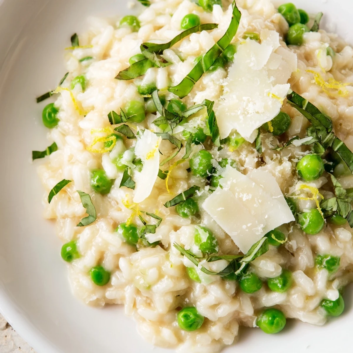 Vibrant green peas scattered throughout tender Arborio rice with melted Parmesan and basil ribbons garnish