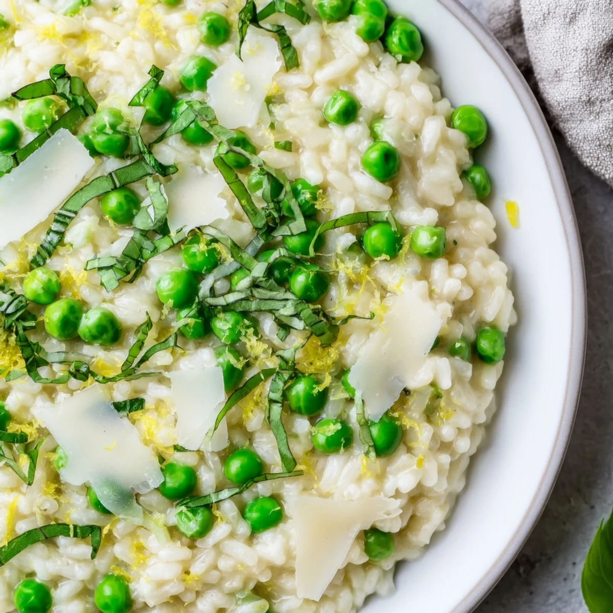 Golden Parmesan sprinkled over spring pea risotto garnished with fresh basil on a rustic wooden table