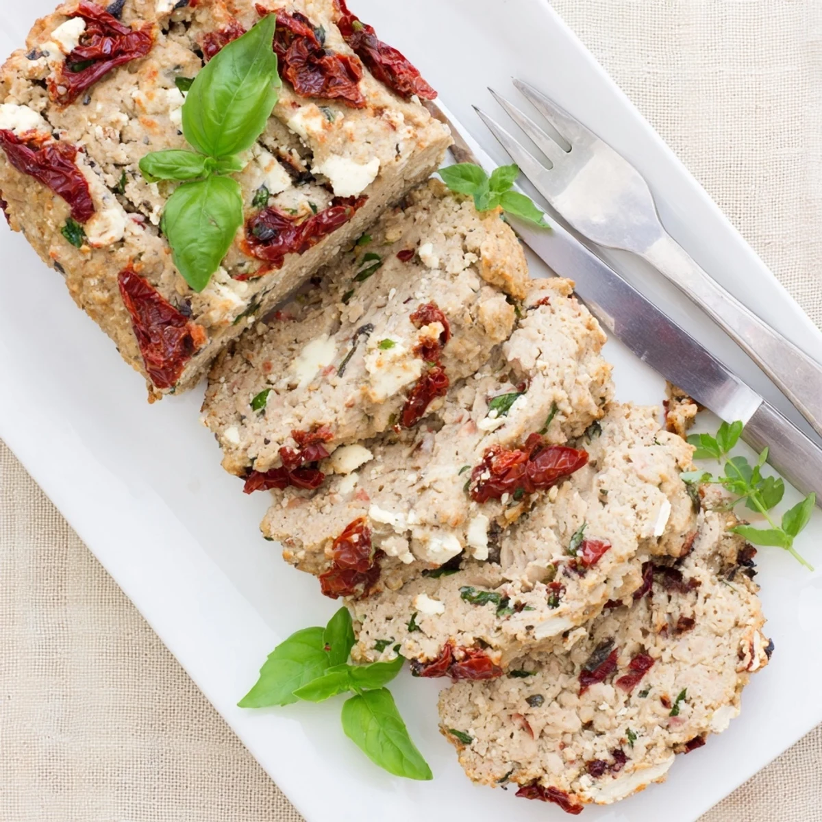 Whole Mediterranean turkey meatloaf in a loaf pan with golden crust and herb garnish