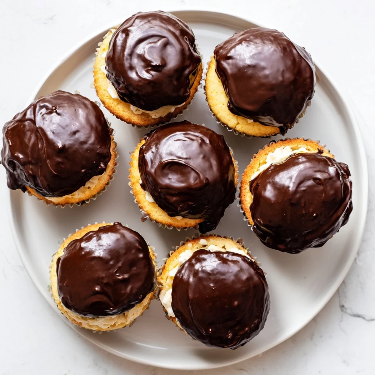 Golden Boston cream pie cupcakes topped with glossy chocolate ganache and filled with creamy vanilla pastry