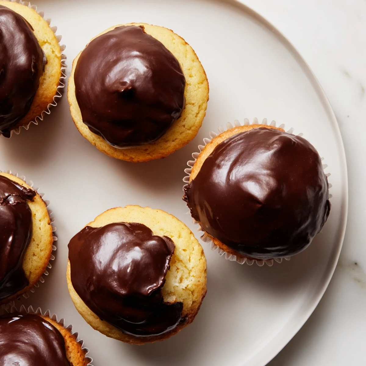 Freshly baked Boston cream pie cupcakes with smooth custard filling and decadent chocolate topping on white plate