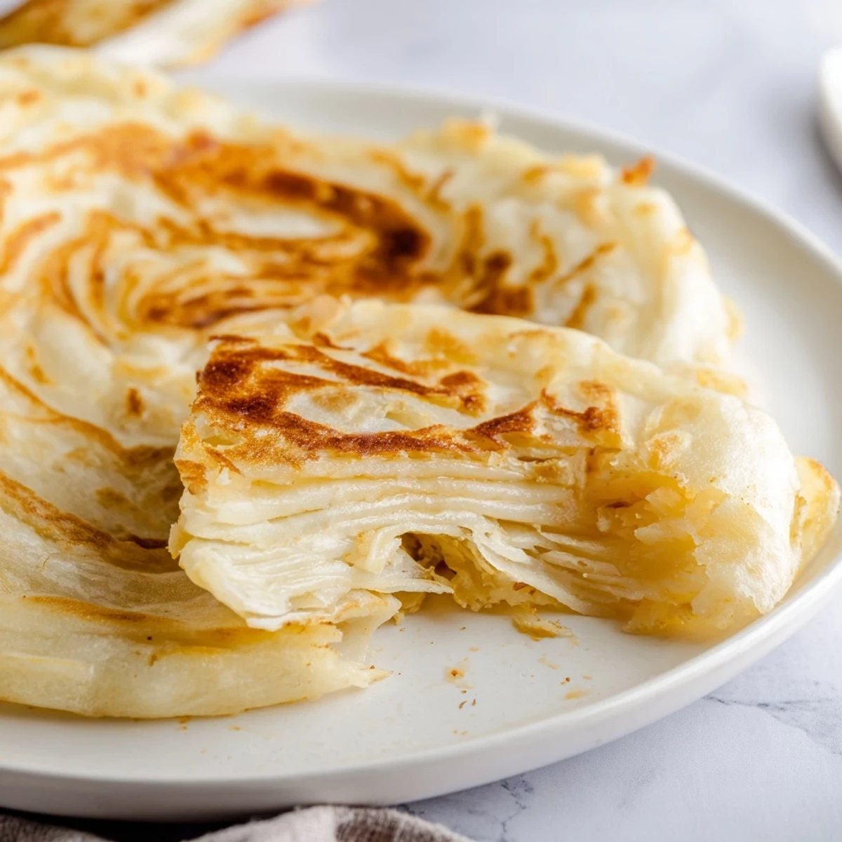 Warm Roti Canai flatbread freshly cooked with ghee displaying signature flaky layers and golden surface