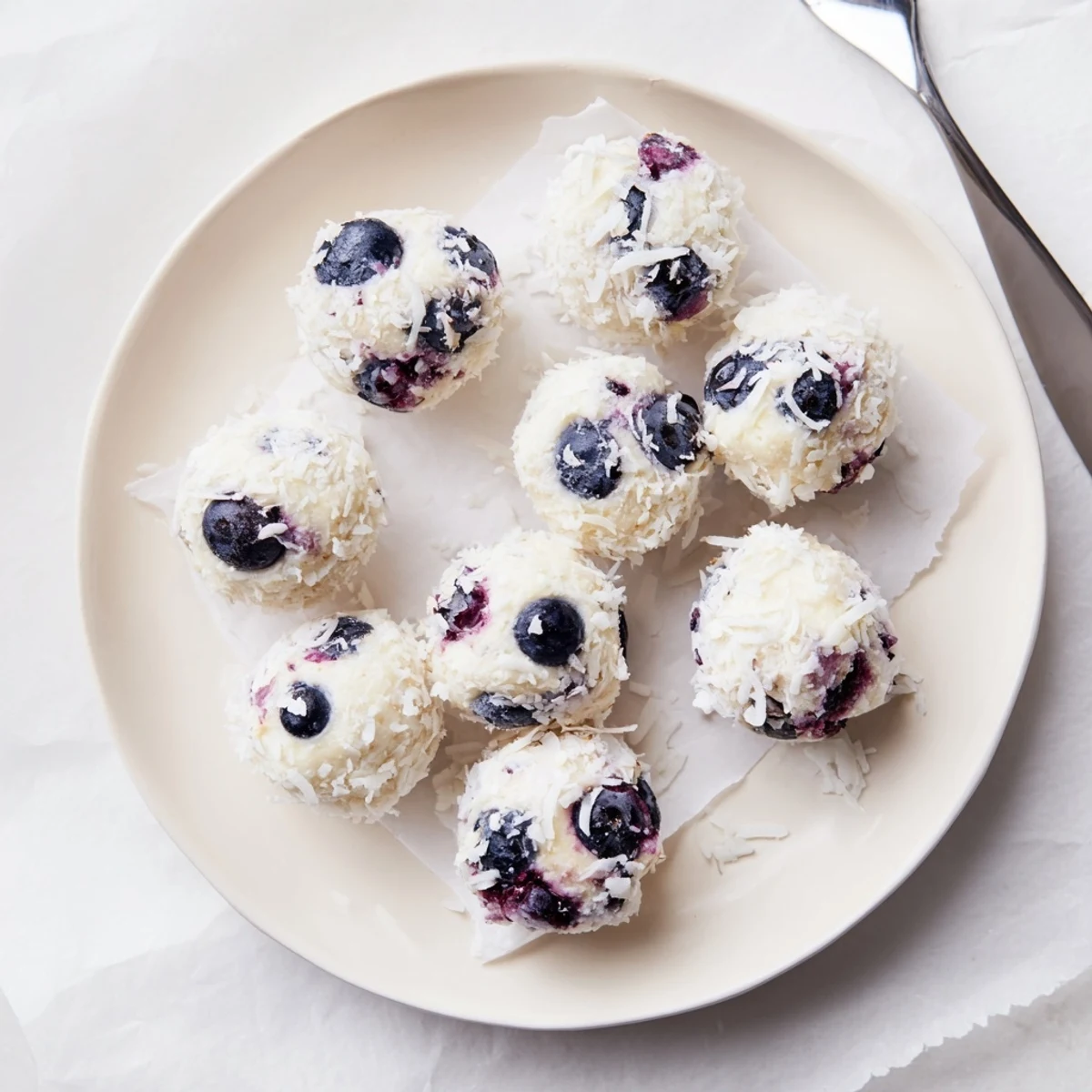 Close-up of bite-sized blueberry cheesecake protein balls on wooden board with shredded coconut coating and visible fruit pieces