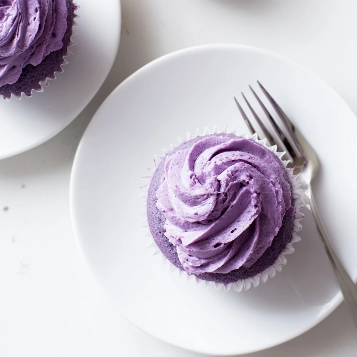Fluffy purple grape soda cupcakes topped with swirls of tangy grape buttercream frosting on a white plate.