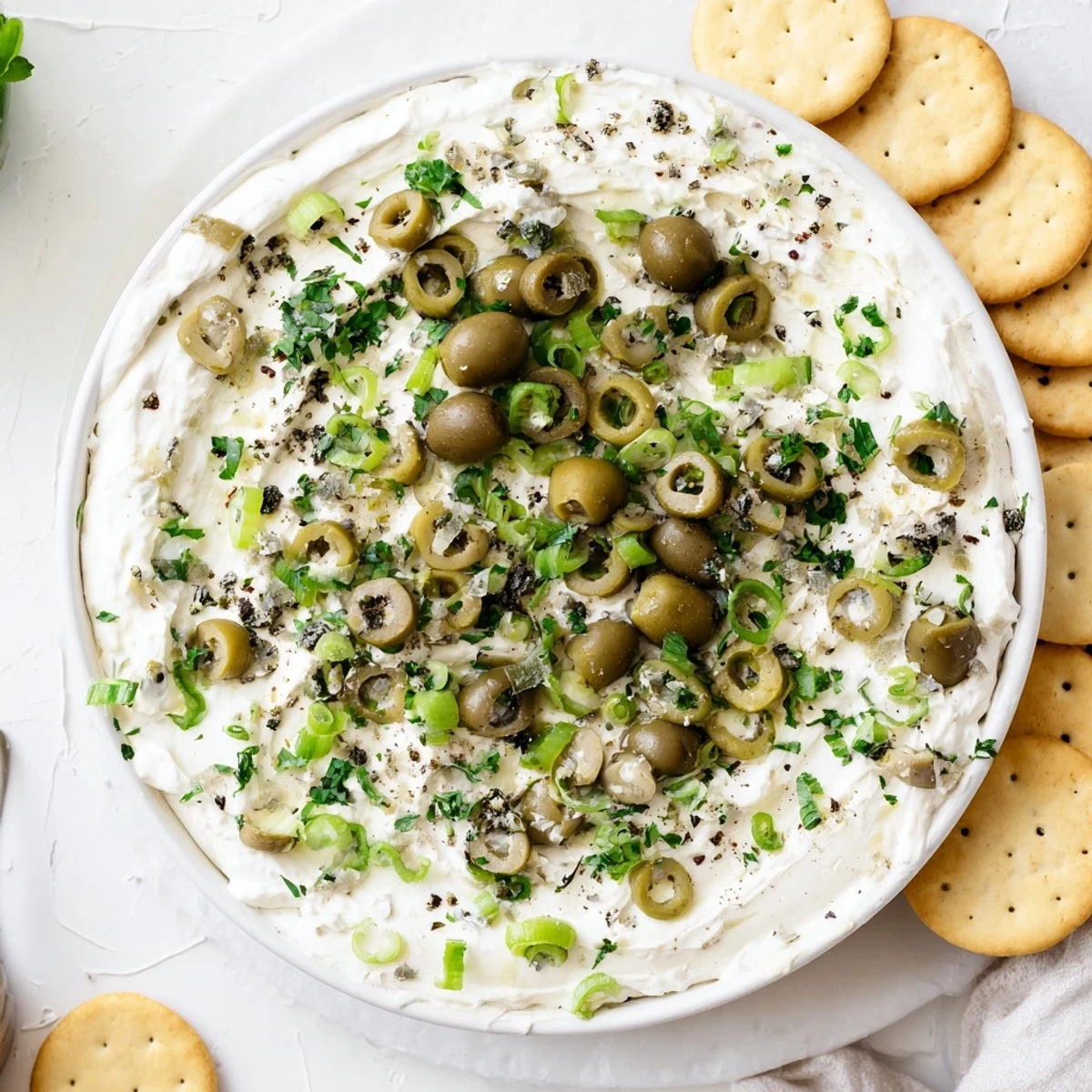 Cream cheese olive dip served in white bowl with crackers and colorful chopped olives