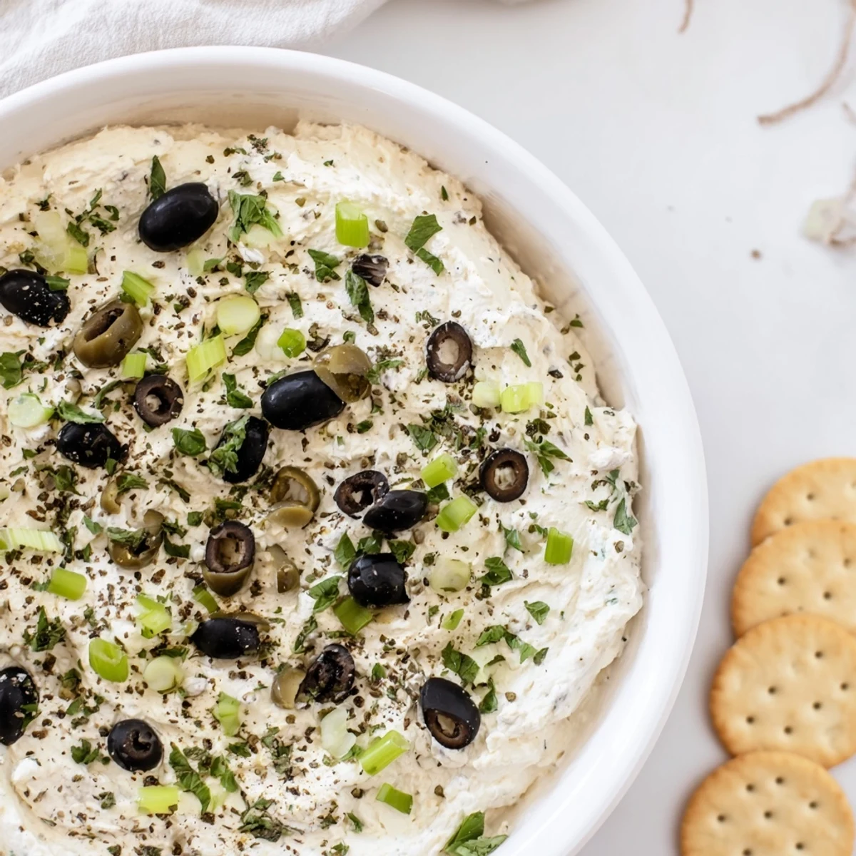 Creamy appetizer dip featuring chopped green and black olives served with crispy crackers