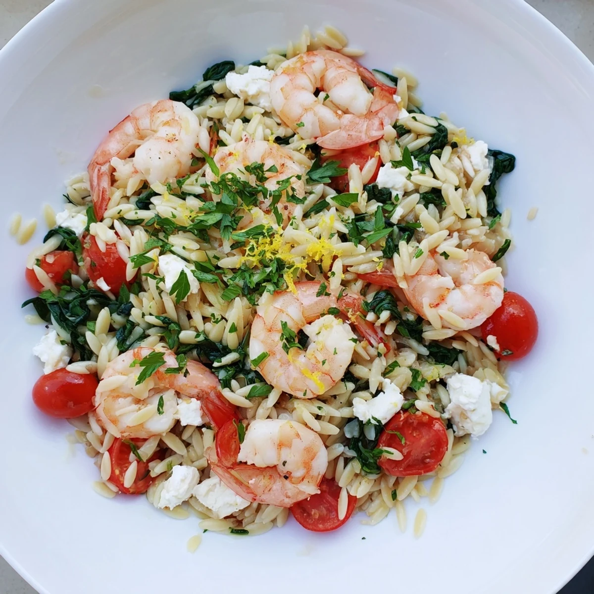 Vibrant bowl of lemon feta orzo shrimp garnished with spinach and cherry tomatoes