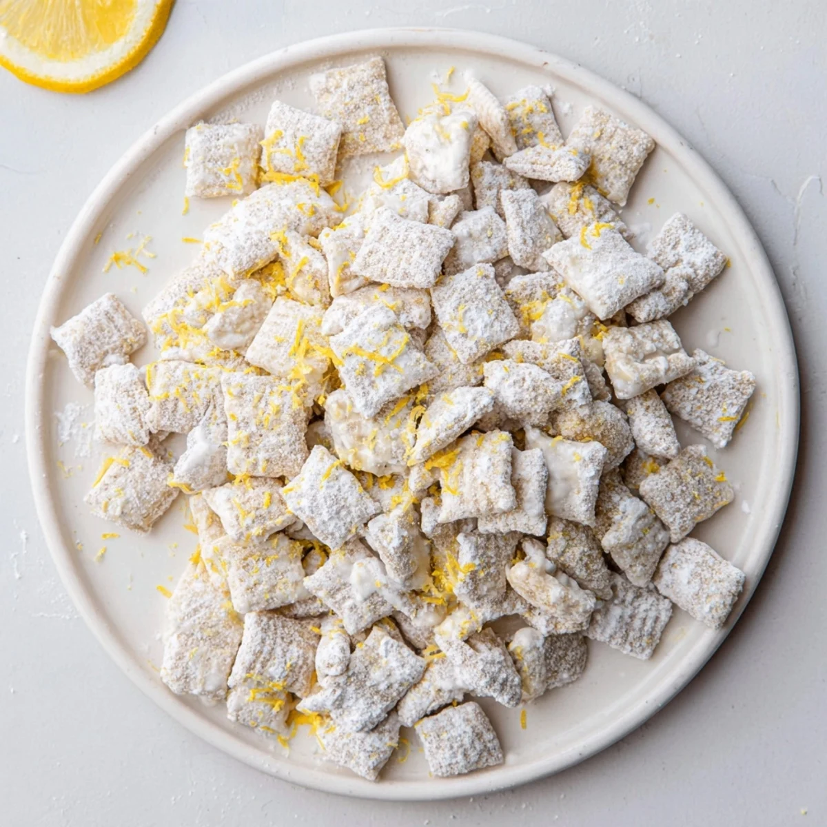 Golden lemonade puppy chow coated in white chocolate and powdered sugar, scattered on a rustic wooden board