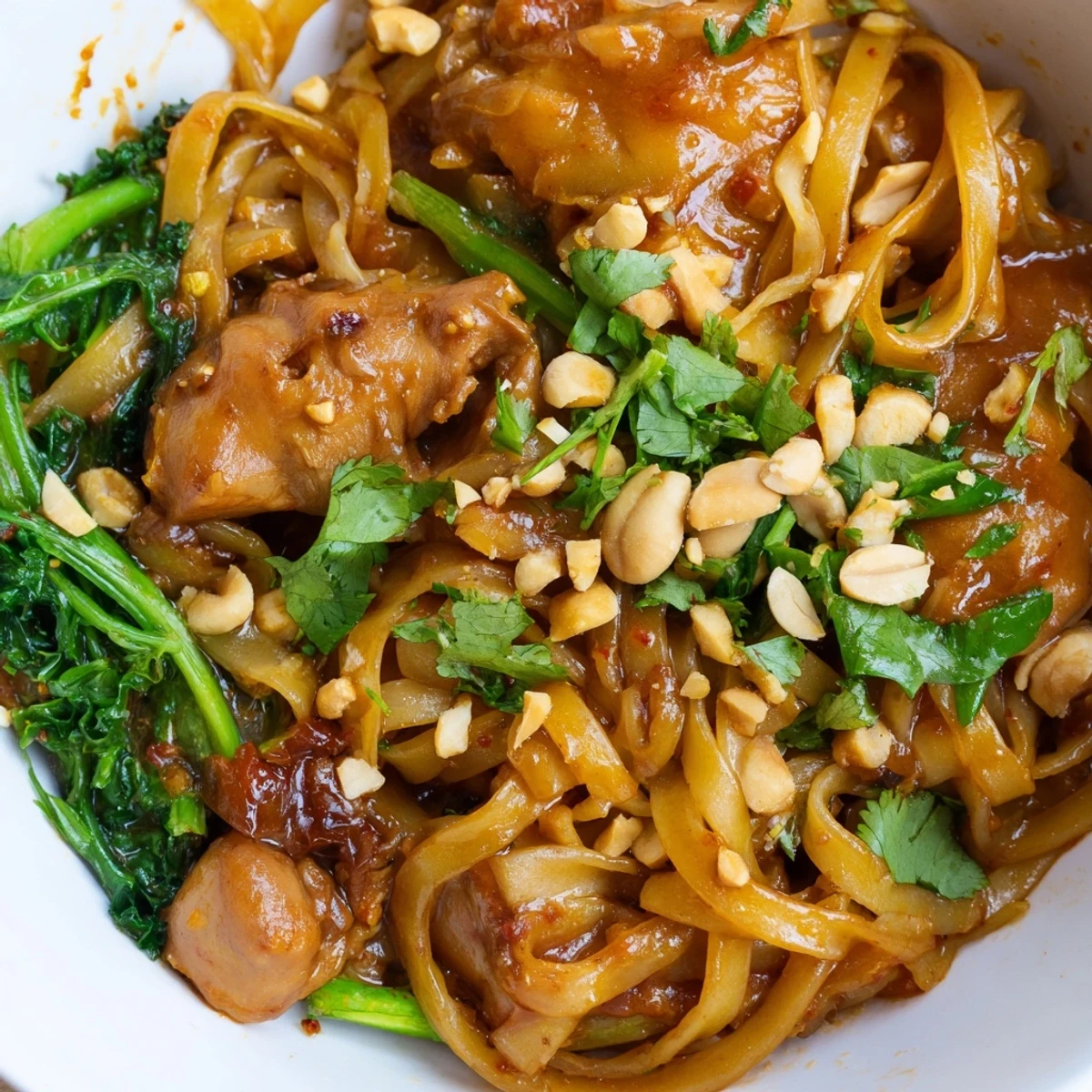 Close-up of Shan noodles recipe showcasing glossy tomato-based chicken sauce, spring onions, coriander, and lime wedges for serving