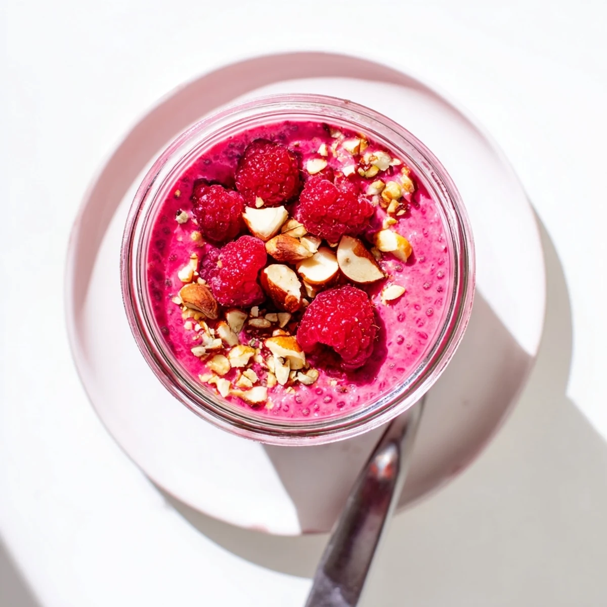 Thick smooth raspberry chia pudding dessert sprinkled with chopped nuts and whole raspberries on top