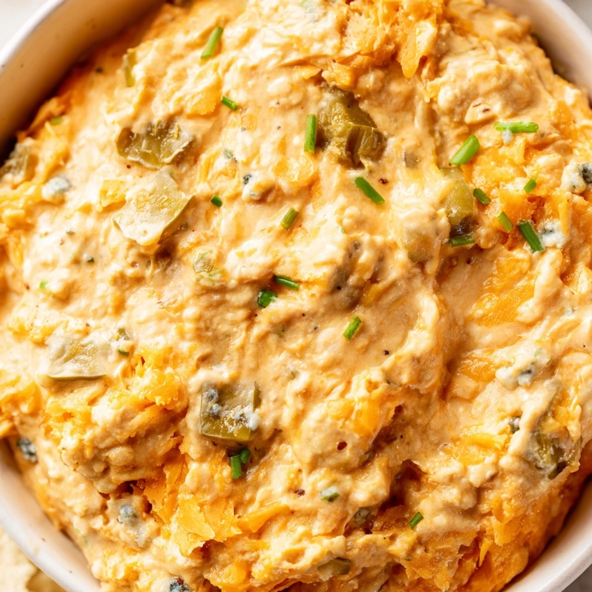 Tangy buffalo pickle dip topped with fresh chives and pickle slices on a rustic serving platter