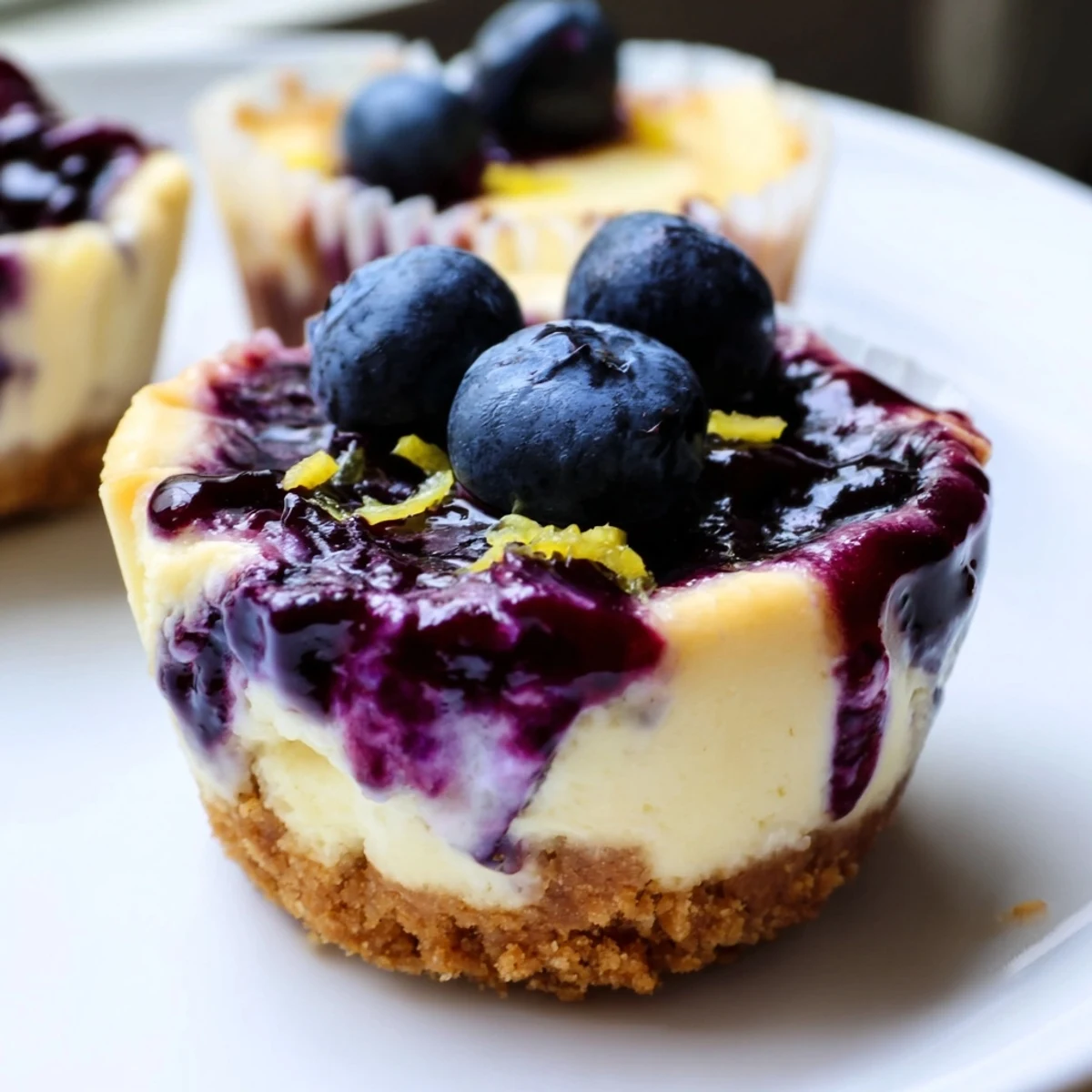 Creamy mini lemon blueberry cheesecakes topped with vibrant purple berry compote on golden crusts