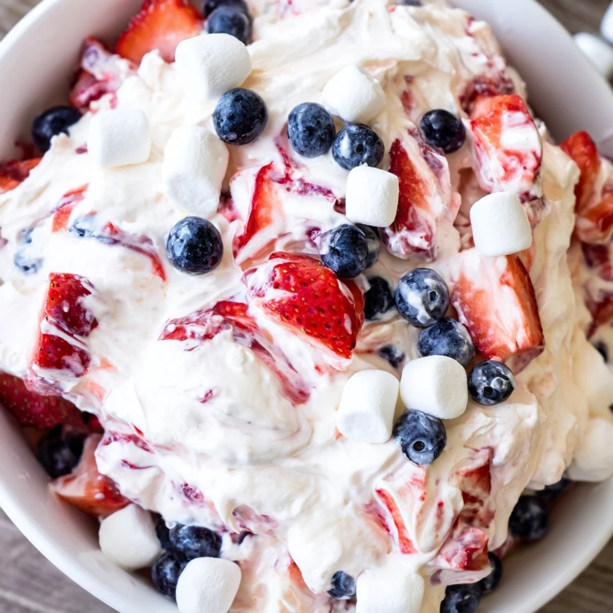 Creamy red white blue cheesecake salad dotted with fresh strawberries and blueberries in a white bowl