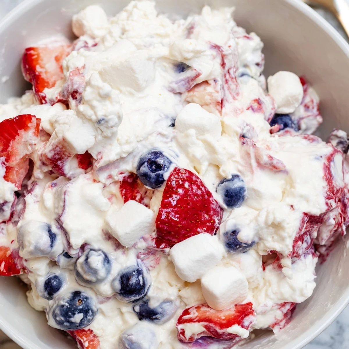 Spoonful of red white blue cheesecake salad coated in fluffy vanilla cream cheese filling