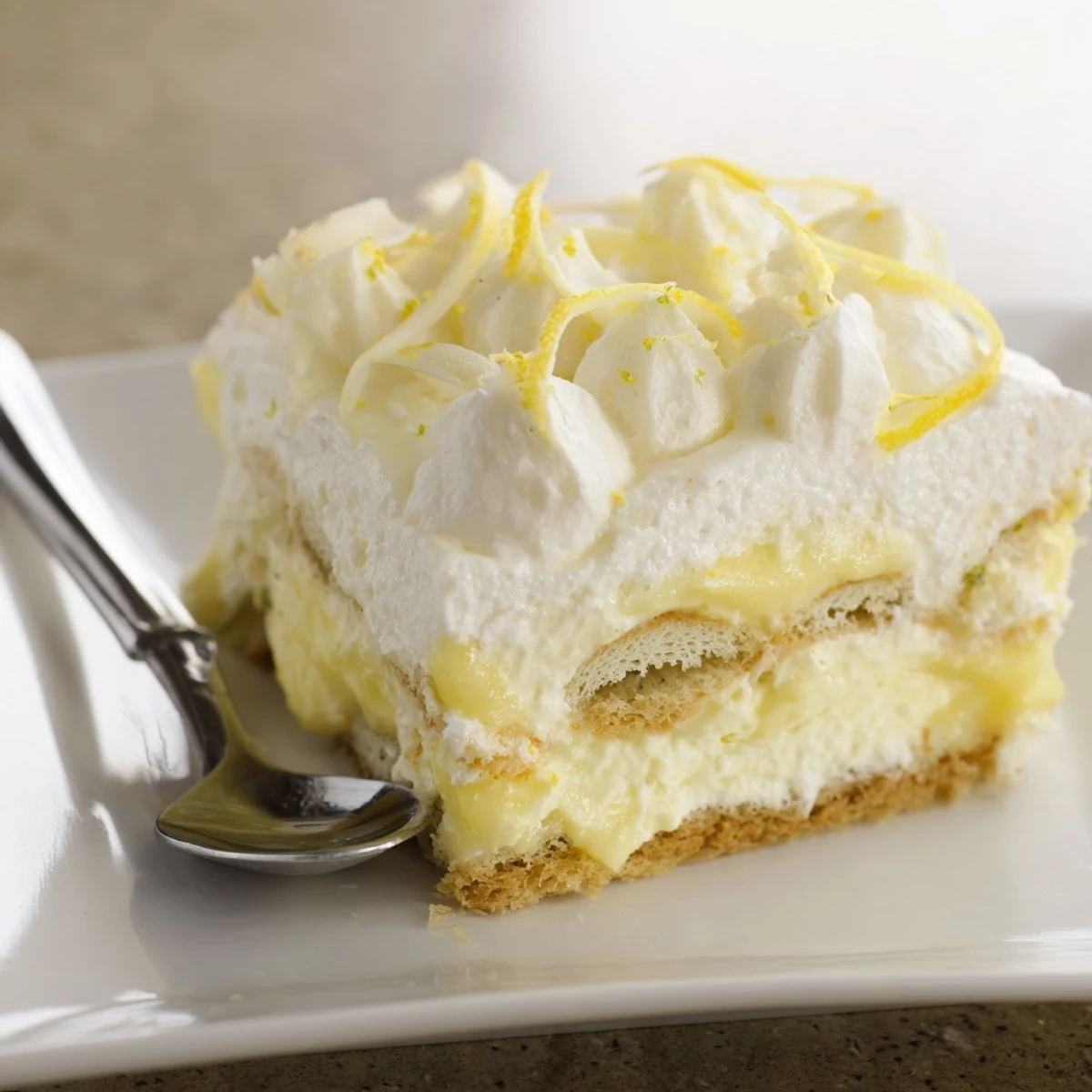 A square dish of zesty lemon tiramisu layered between syrup-soaked ladyfinger biscuits