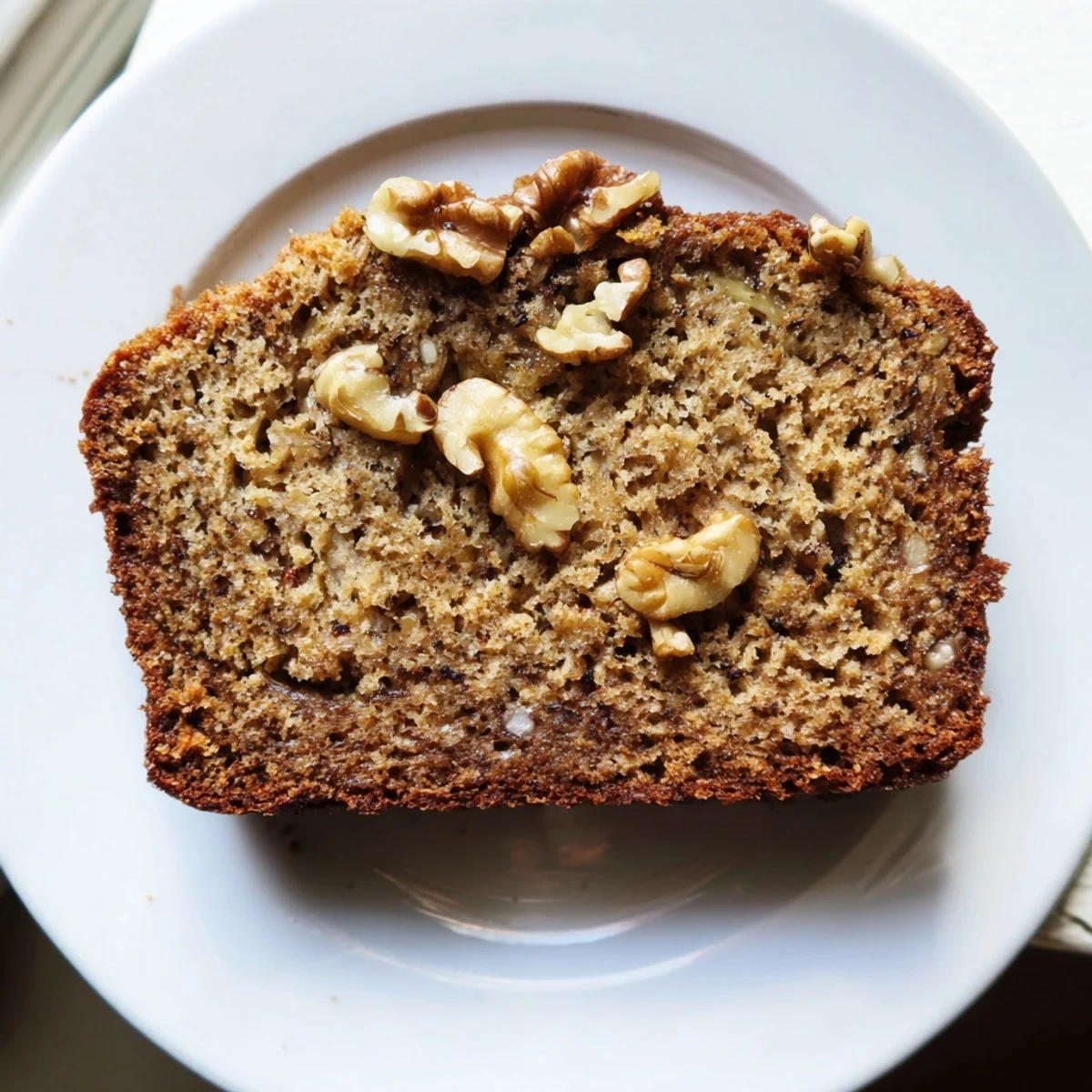 Golden banana nut bread loaf sliced on a rustic wooden board, topped with walnuts