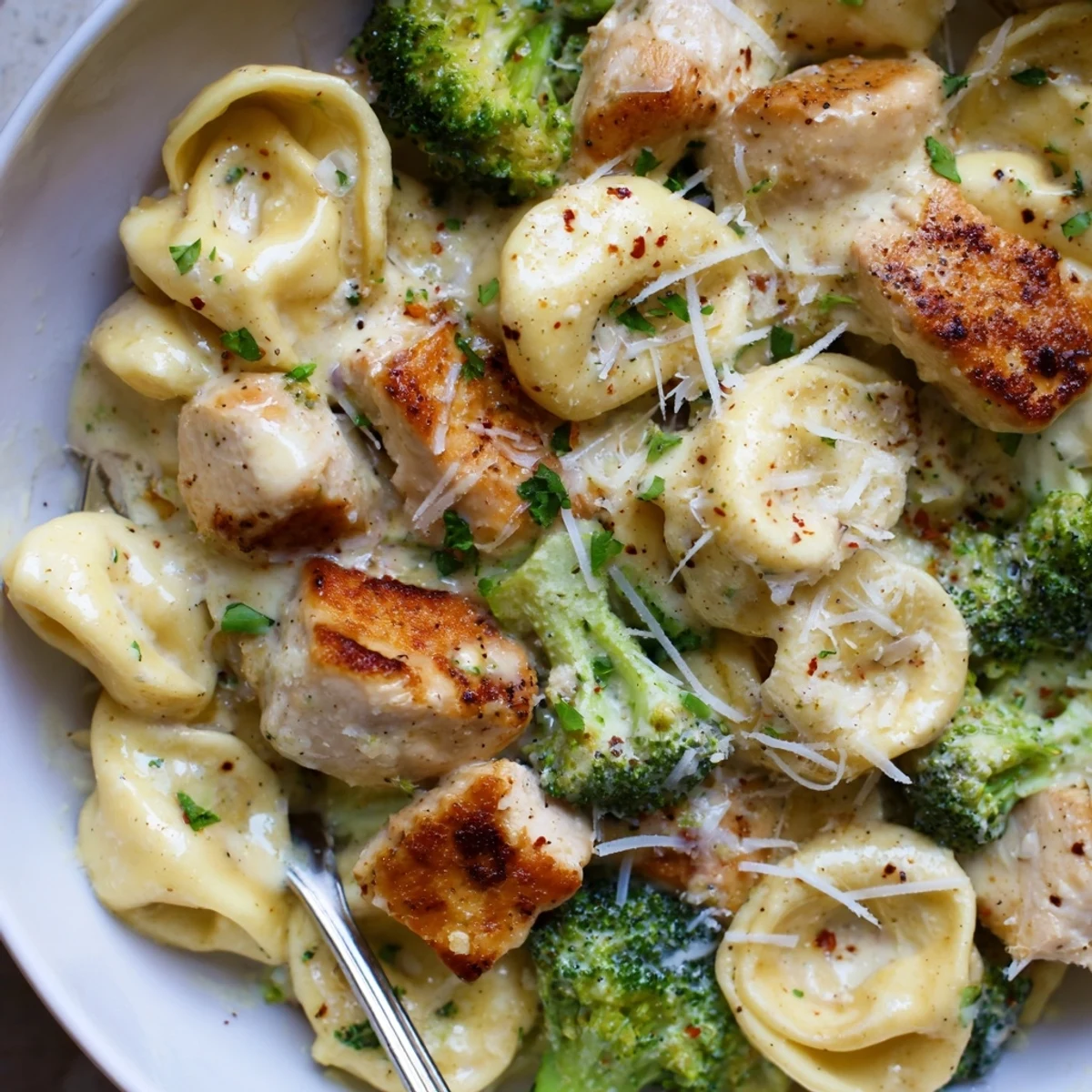Bowl of Creamy Garlic Parmesan Tortellini Chicken Broccoli Recipe topped with parsley.