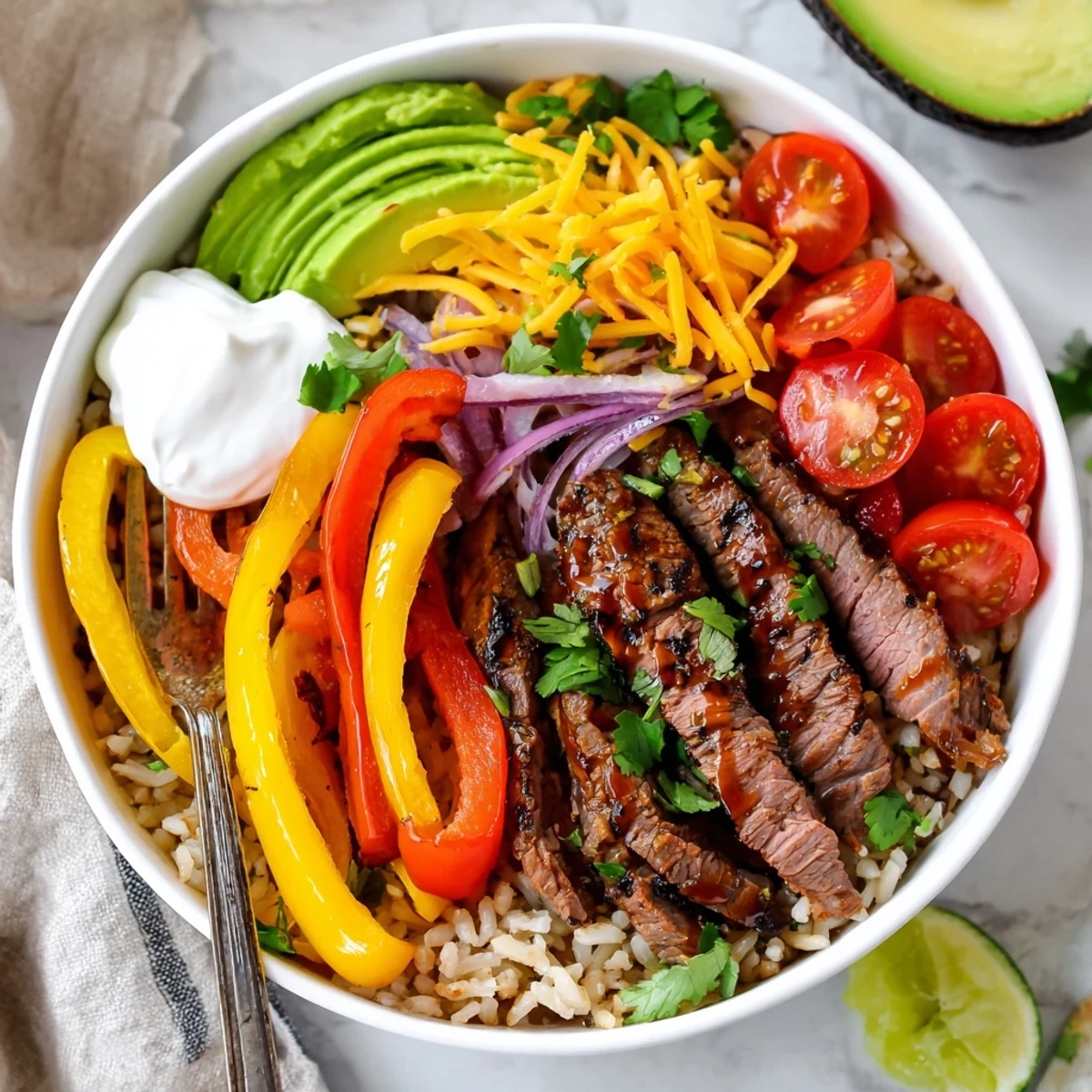 Sliced avocado and lime surround Steak Fajita Power Bowls in rustic bowl