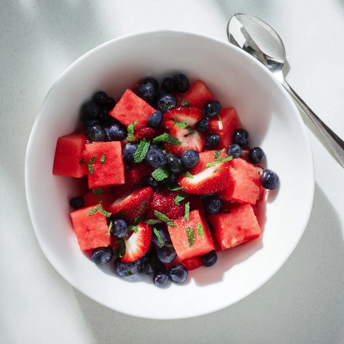 Fresh watermelon fruit salad bowl with strawberries, blueberries, mint, and lime zest drizzle
