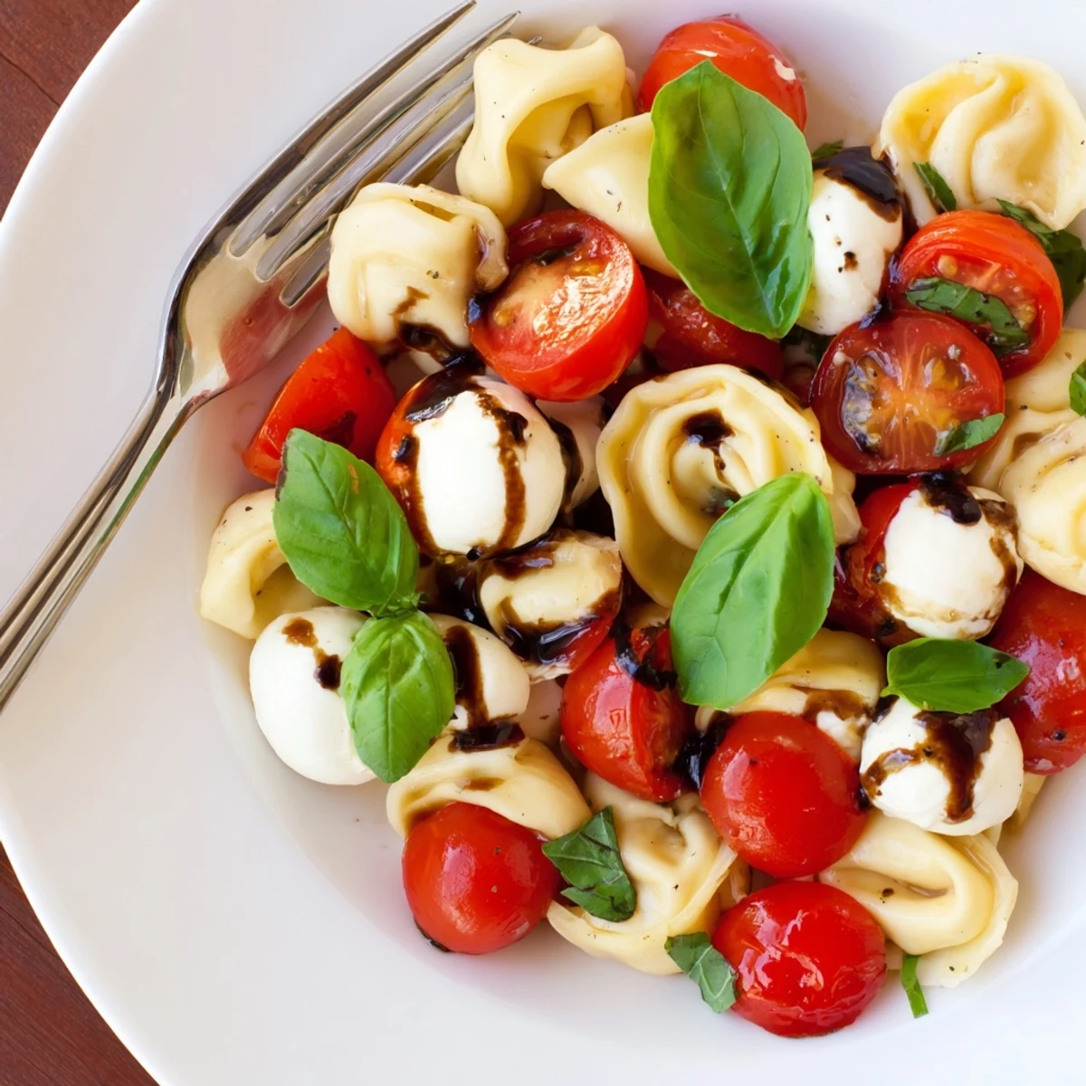 Fresh Italian pasta salad showcasing al dente tortellini with halved mozzarella balls, juicy tomatoes, and torn basil in a white serving bowl