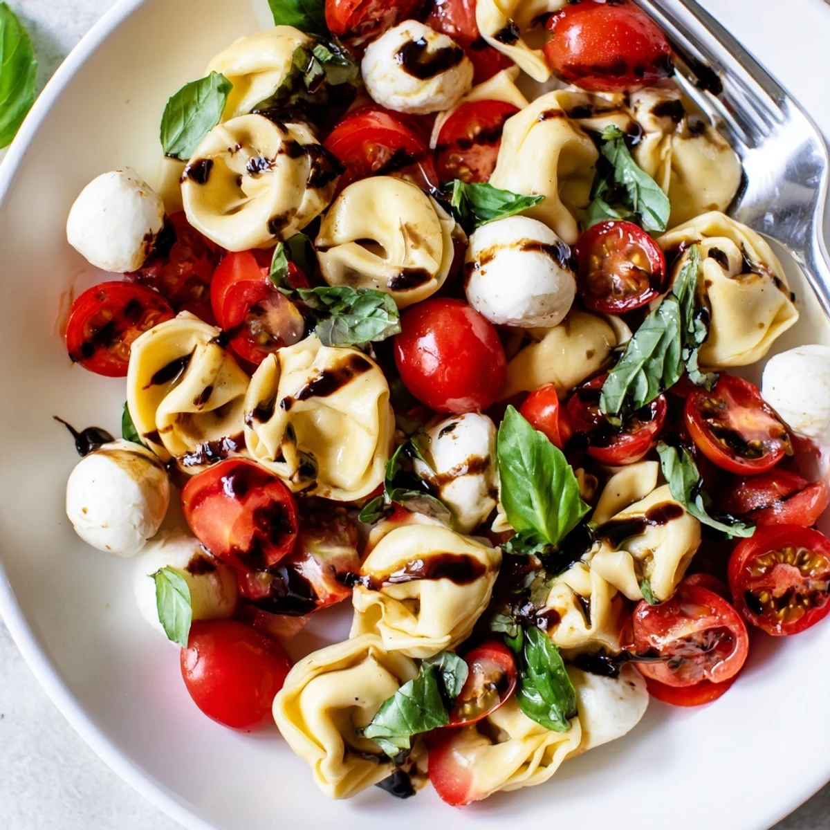 Colorful Tortellini Caprese Salad bowl featuring tender cheese pasta, cherry tomatoes, and fresh basil leaves drizzled with balsamic glaze