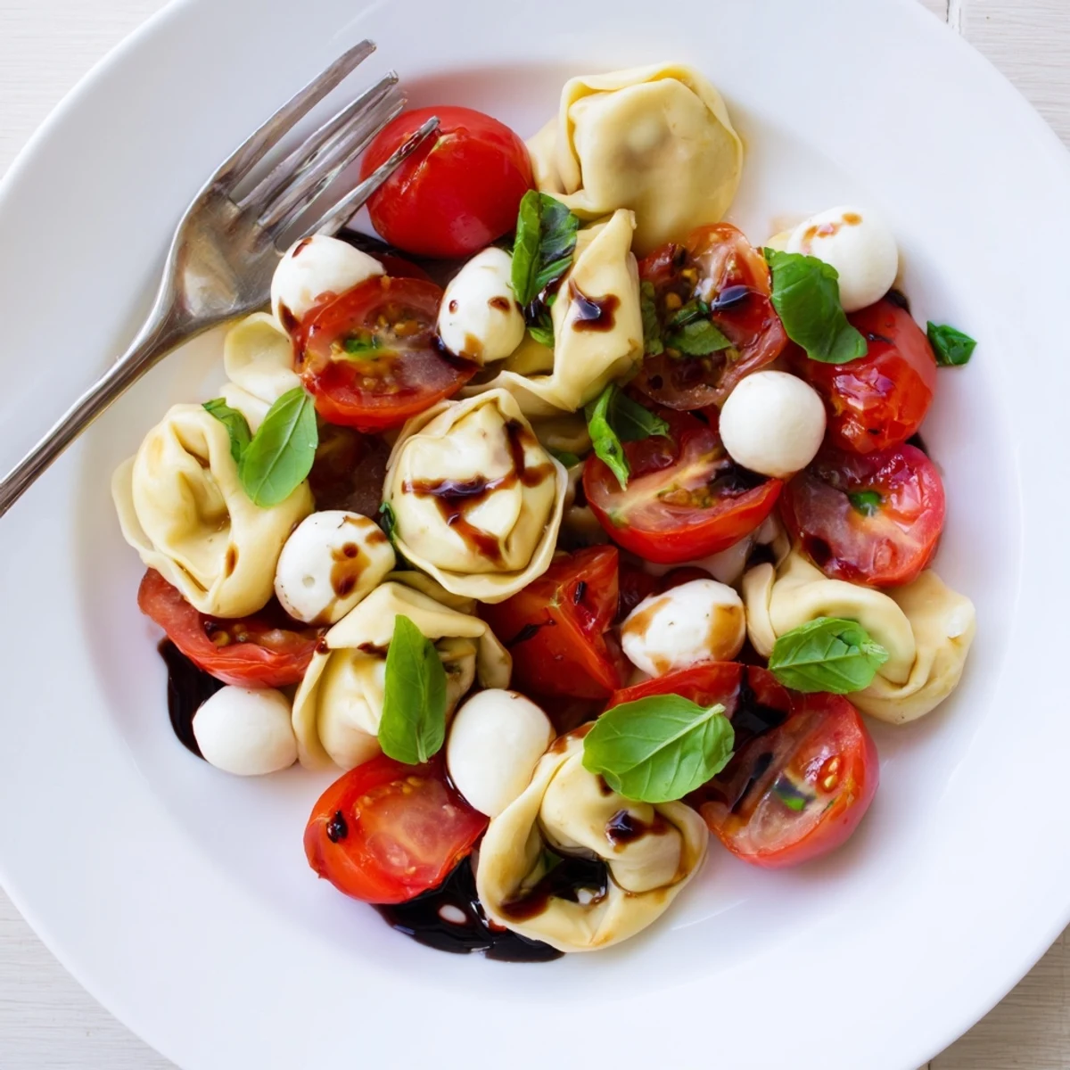 Vibrant summer Tortellini Caprese Salad plated with glossy cheese-filled pasta, ripe red cherry tomatoes, and green basil accents under olive oil dressing