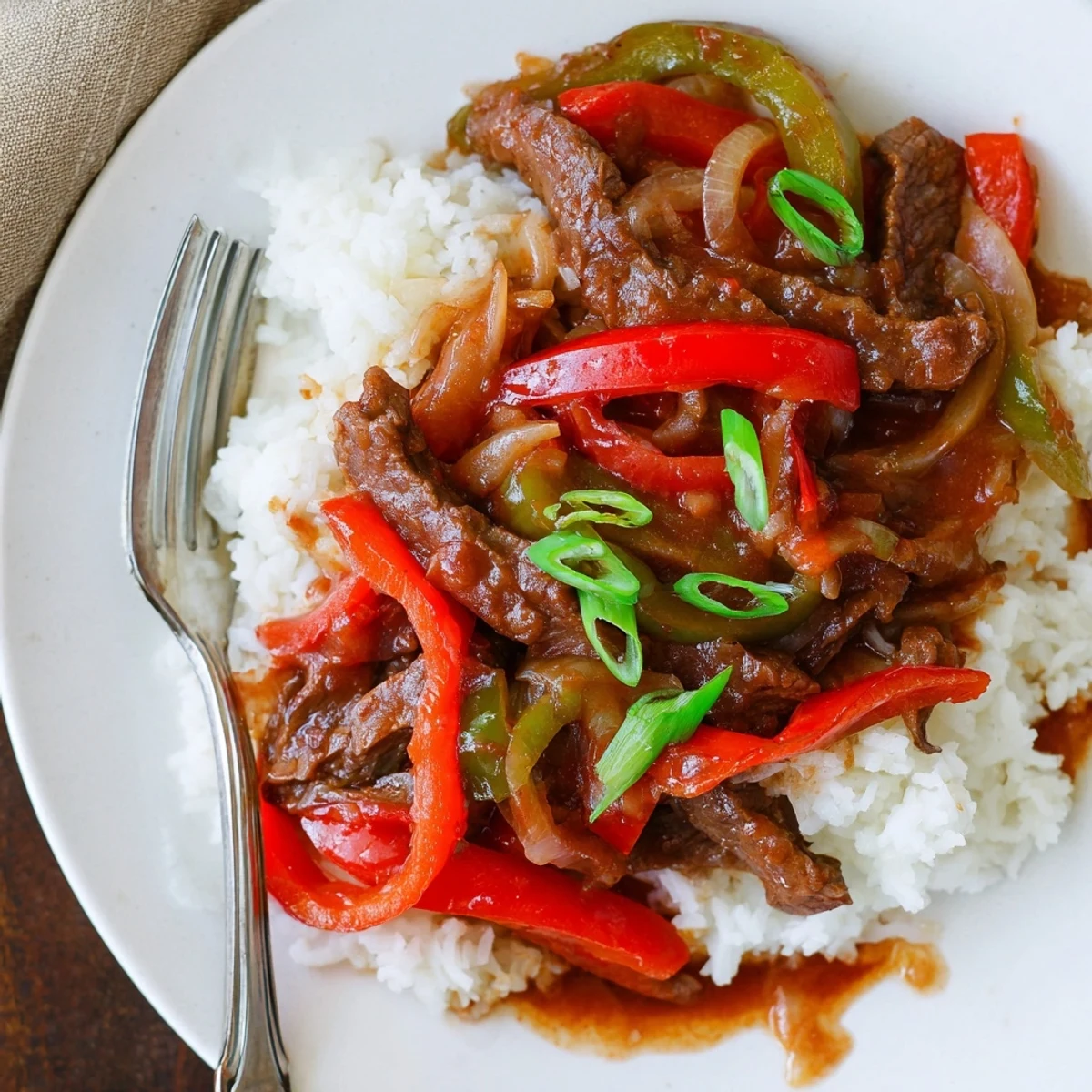 Slow Cooker Pepper Steak served over white rice with tender beef strips and colorful bell peppers in glossy savory sauce