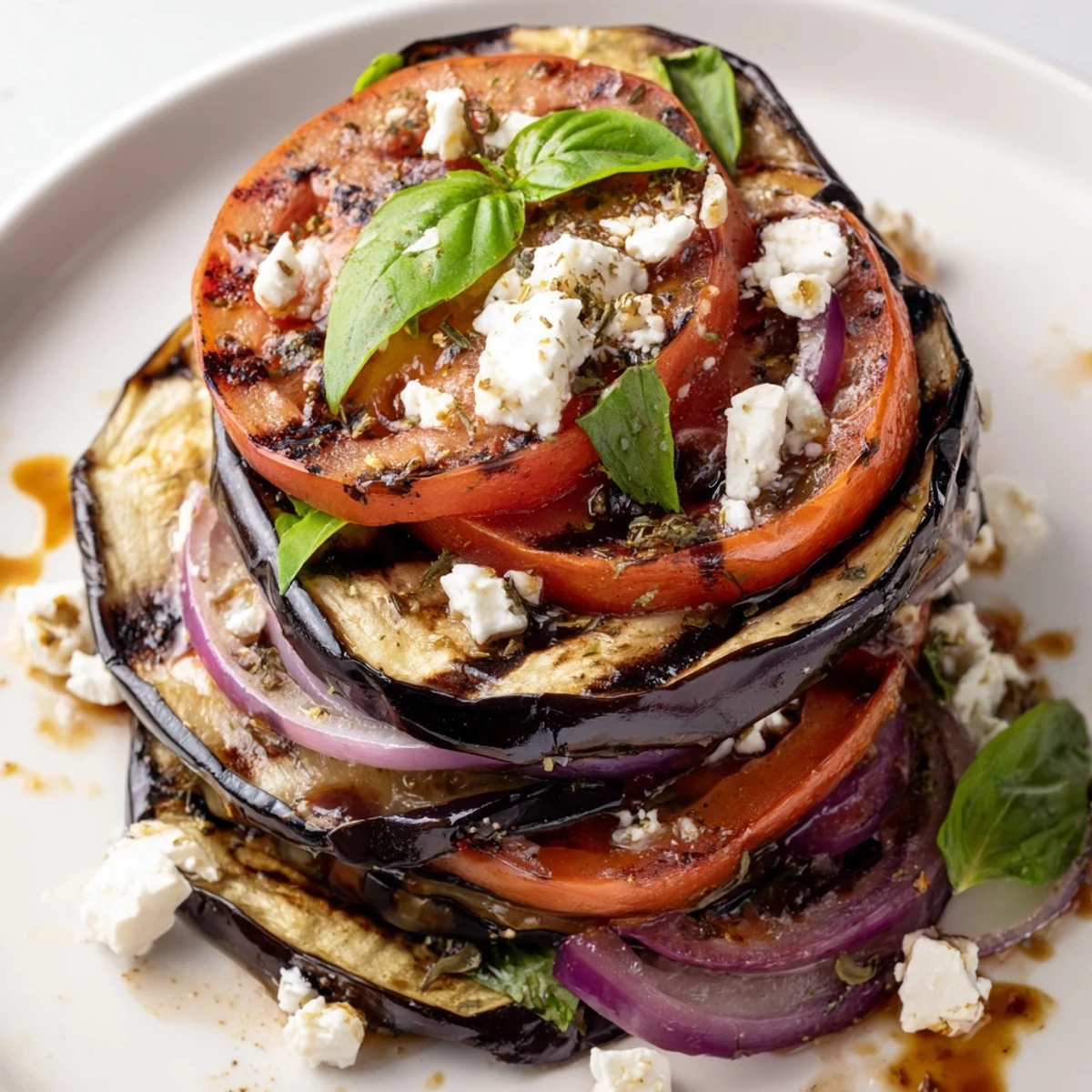 Tender grilled tomato eggplant layered with red onion and herbs served warm Mediterranean style