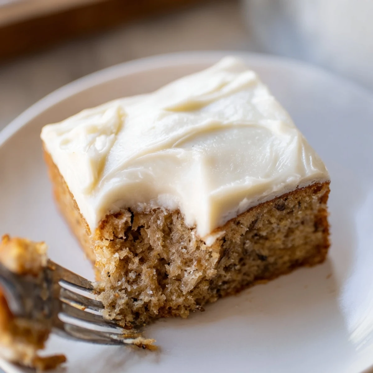 Moist brown butter banana cake sliced thick with generous cream cheese frosting on a rustic plate