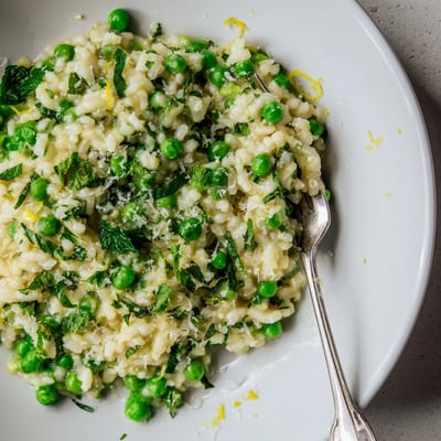 Vibrant green peas scattered throughout golden Arborio rice finished with butter and lemon zest garnish