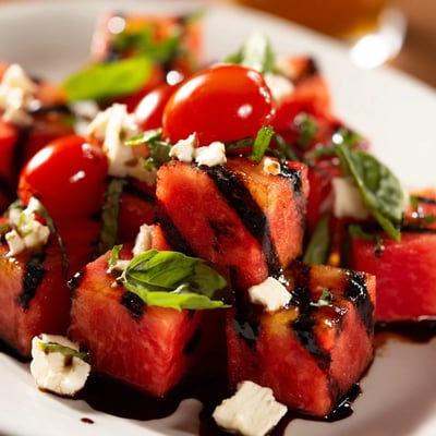 Grilled watermelon salad with cherry tomatoes, red onion, and balsamic glaze drizzle